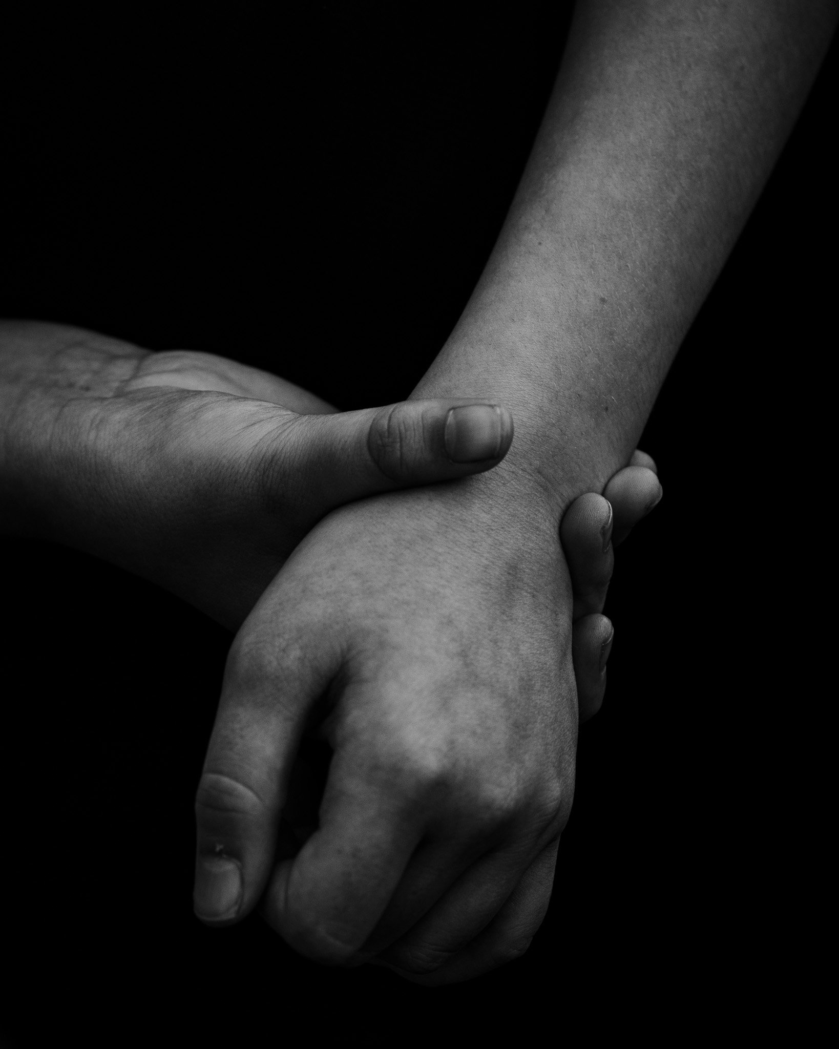 Two hands, one clasping the other, in black and white against a dark background.