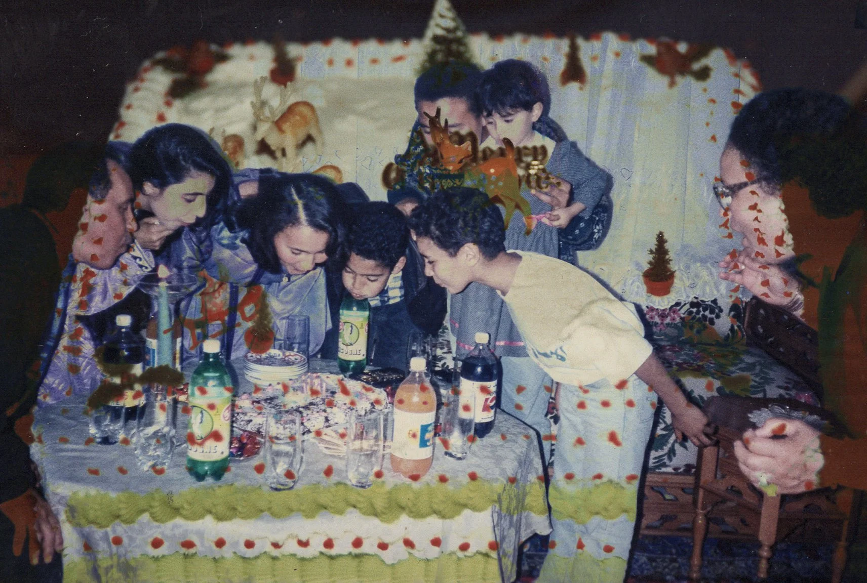 Children gathered around a birthday cake on a decorated table, blowing out candles.