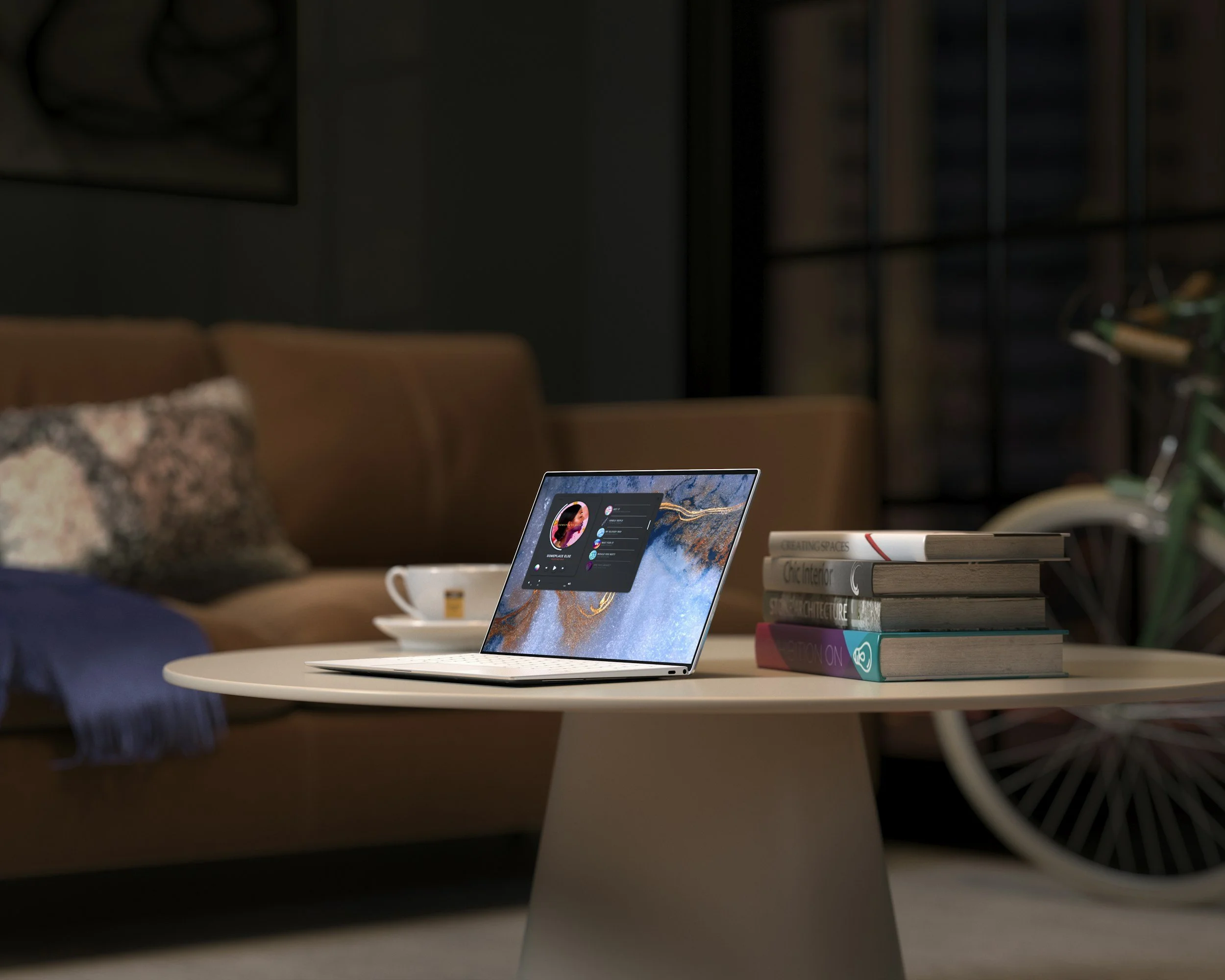A laptop on a white table with a mountain landscape wallpaper on the screen and a digital meeting interface open, beside a stack of books and a white coffee mug, in a cozy living room with a couch, pillows, and shelving in the background.