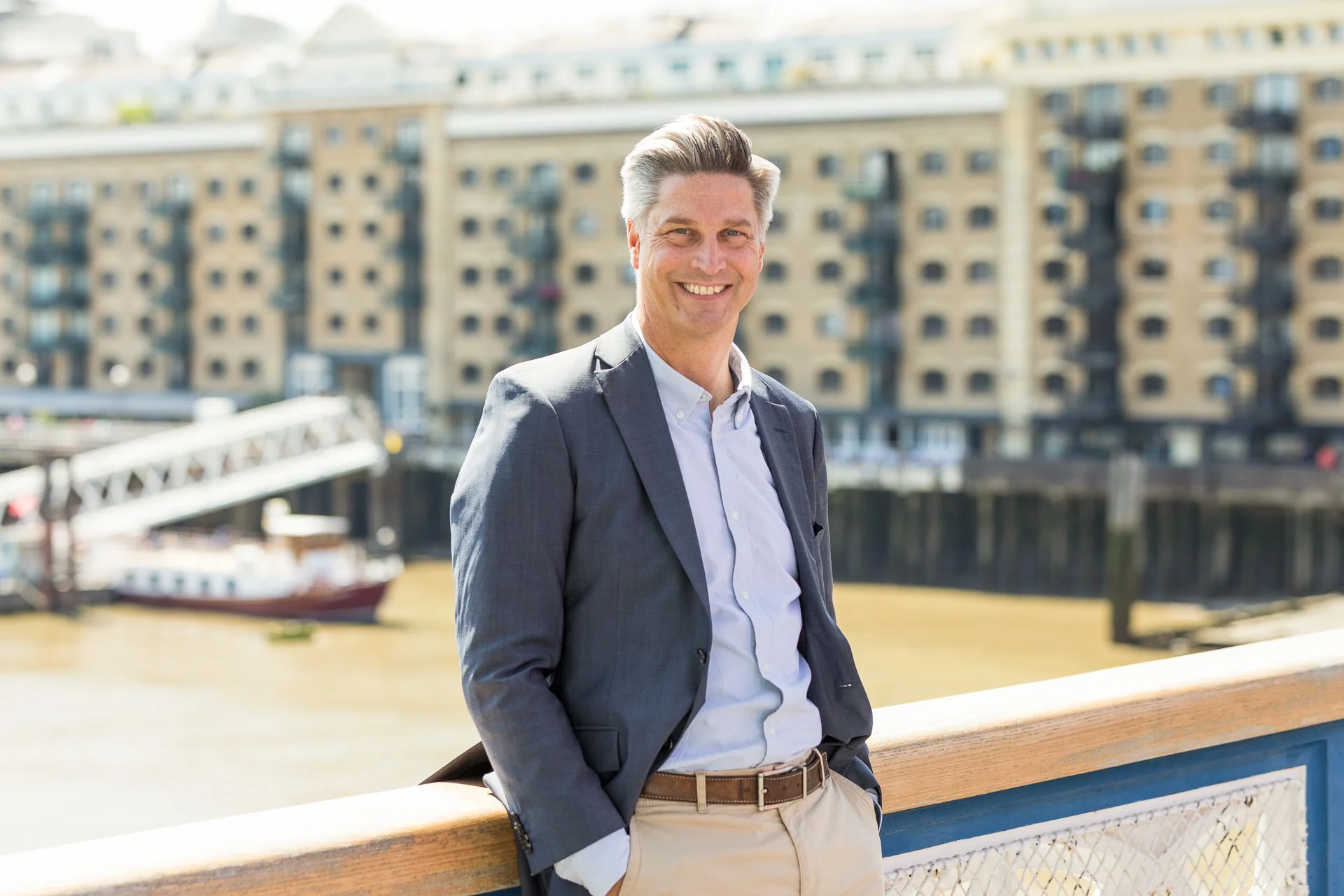 A man smiling, wearing a blazer in front of Butlers Wharf