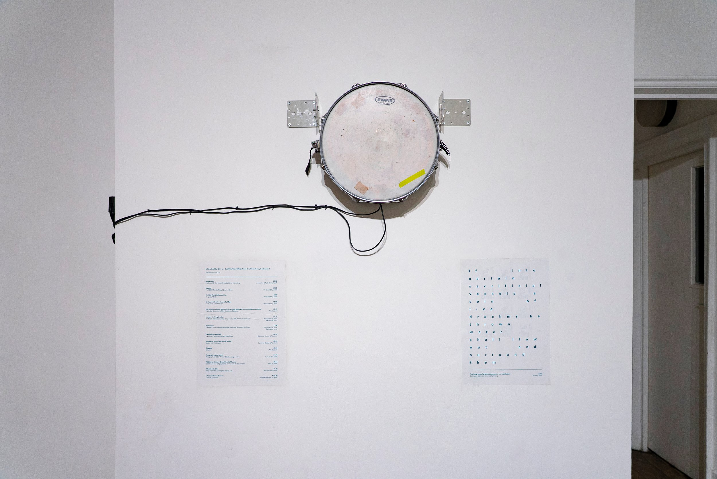 Wall-mounted drum with electrical wire, located in a room with partially visible doorway and two large prints on the wall below it.
