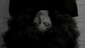 Upside-down portrait of a woman with curly hair and a neutral expression, looking directly at the camera.