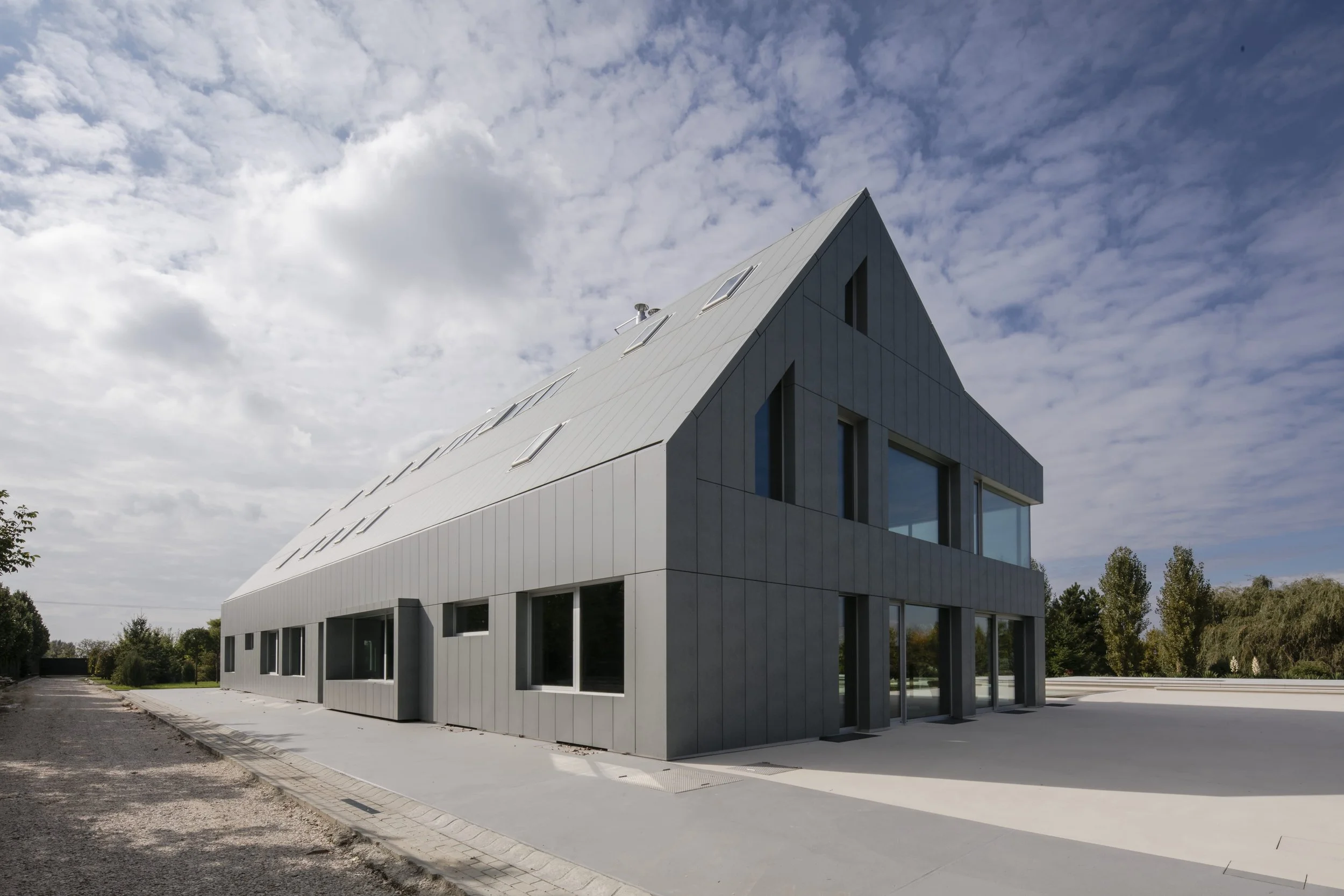 Modern building with a sloped roof and large windows under a partly cloudy sky.