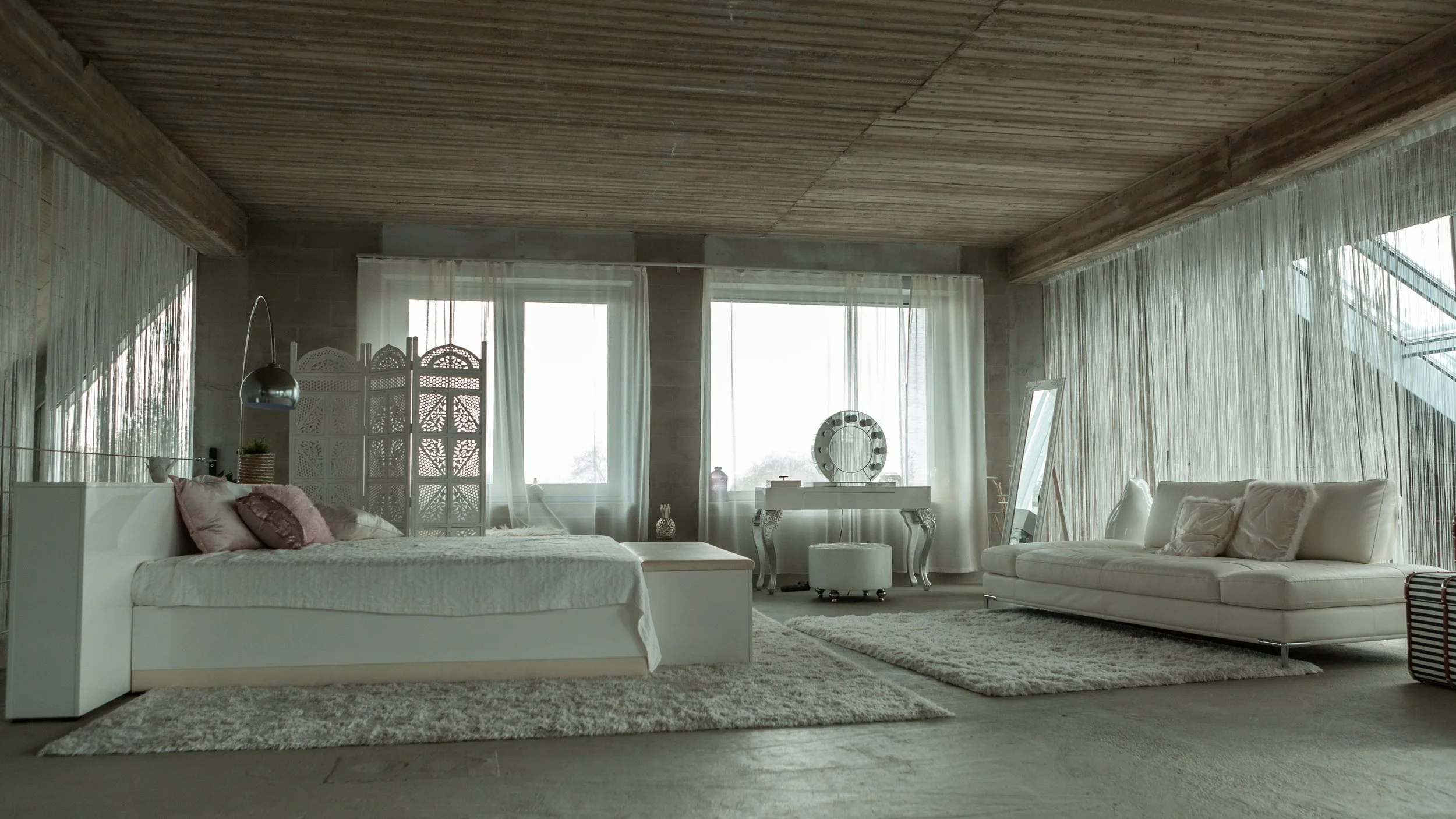Spacious bedroom with white furniture, large windows with sheer curtains, and a mix of rugs and decor in neutral tones.