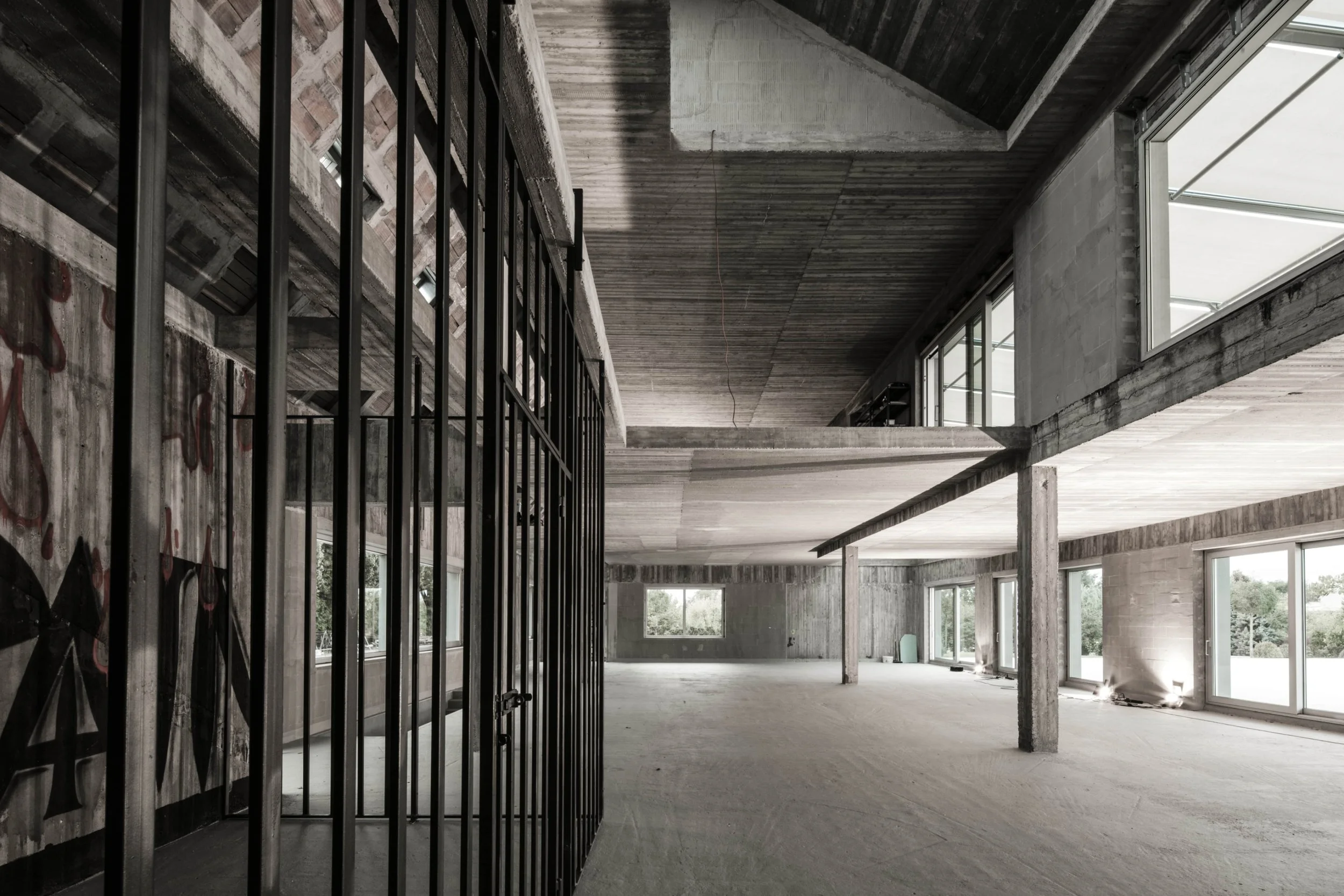 Interior of an unfinished building with exposed concrete walls, large windows, and a metal gate.