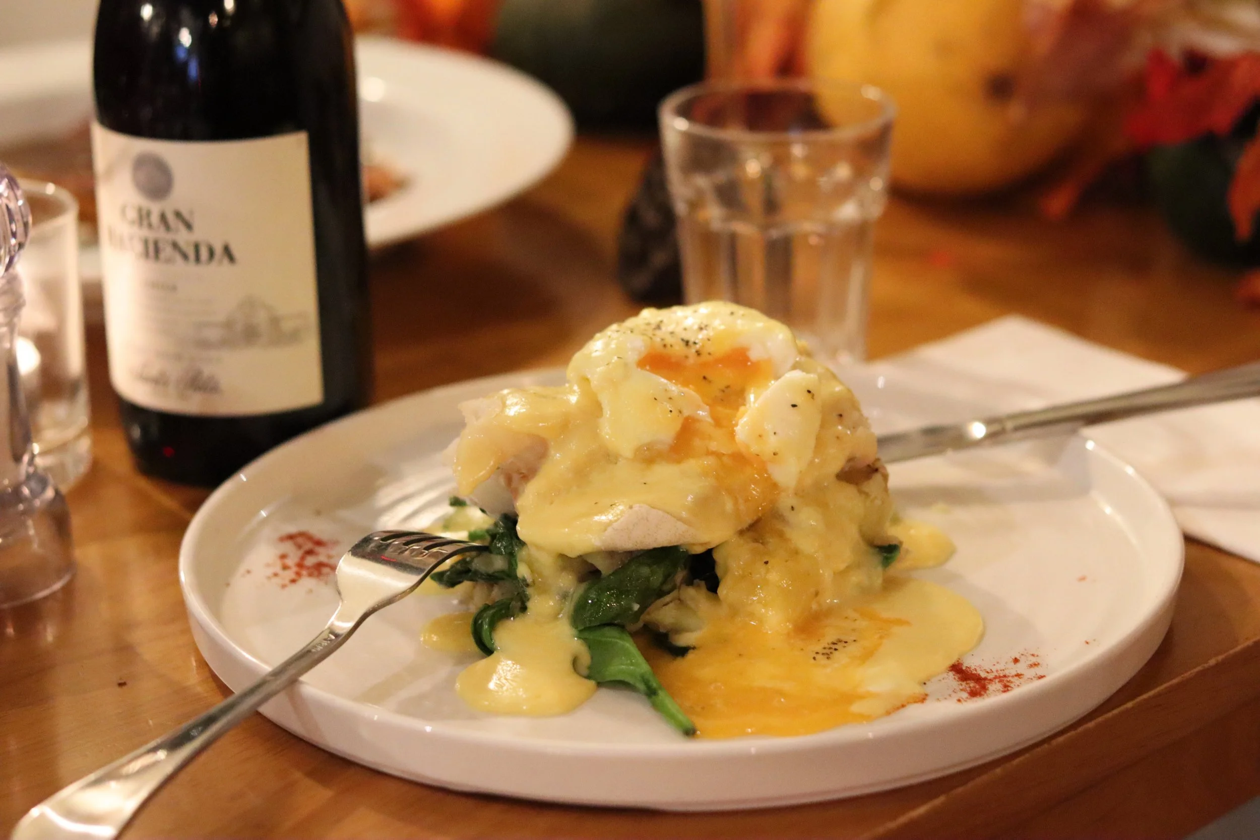 Mashed potatoes topped with melted cheese and a soft-boiled egg on a white plate, with a fork and a glass of water, on a wooden table.