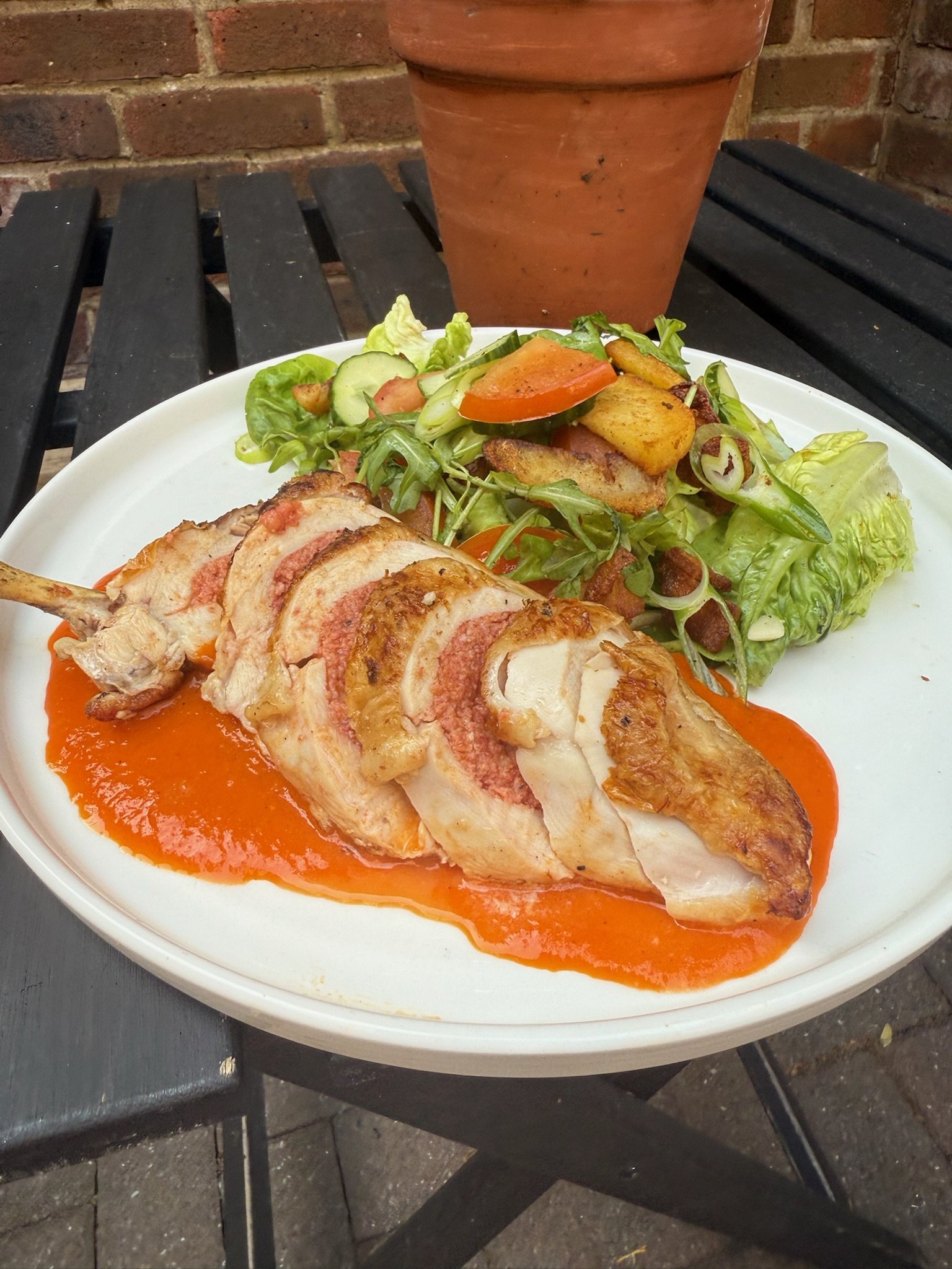 Plated dish with sliced chicken breast topped with red sauce, served with a side salad of mixed greens and vegetables, on a white plate.