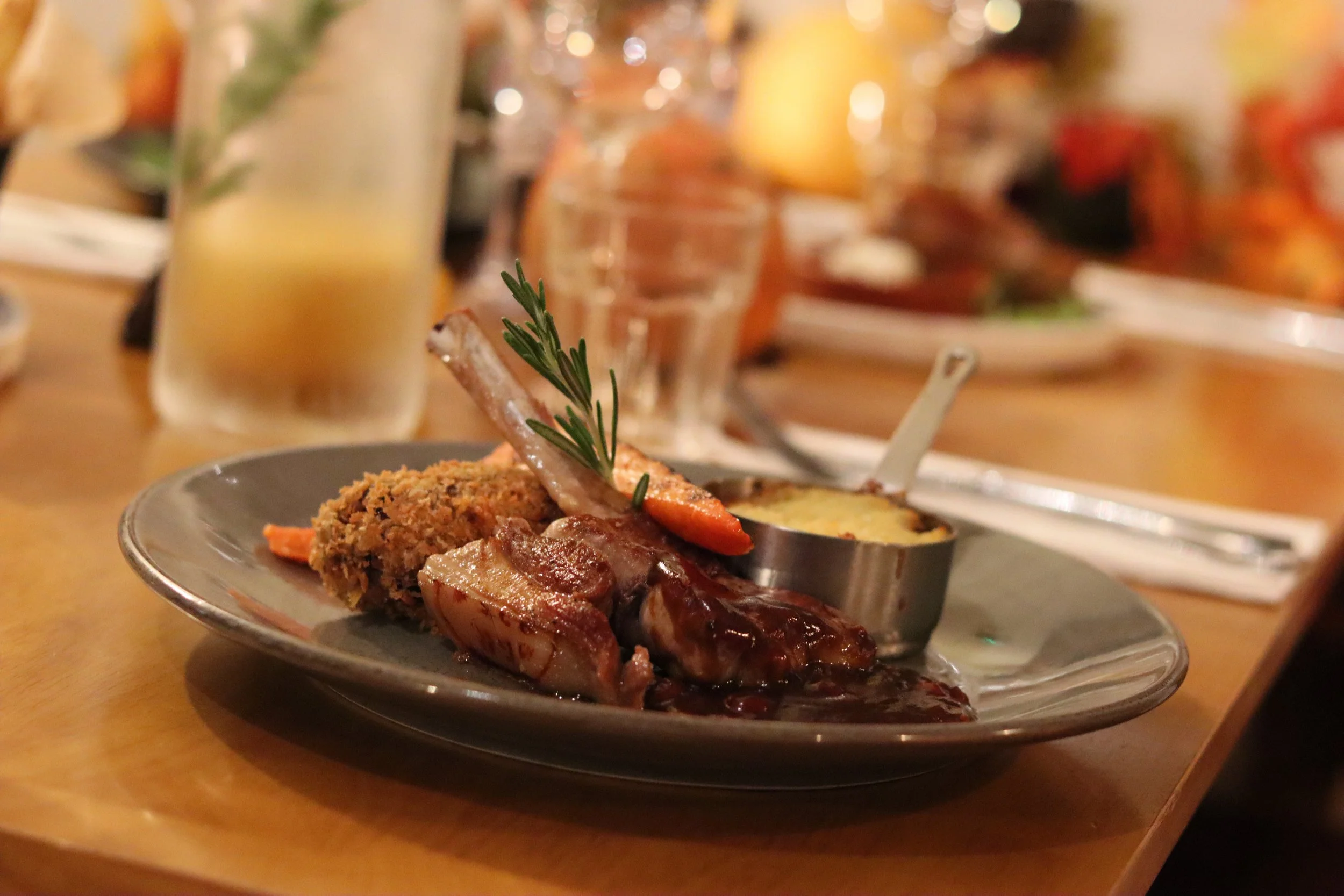 A plate of various meats with sauce and garnished with a sprig of rosemary, set on a wooden table at a restaurant.