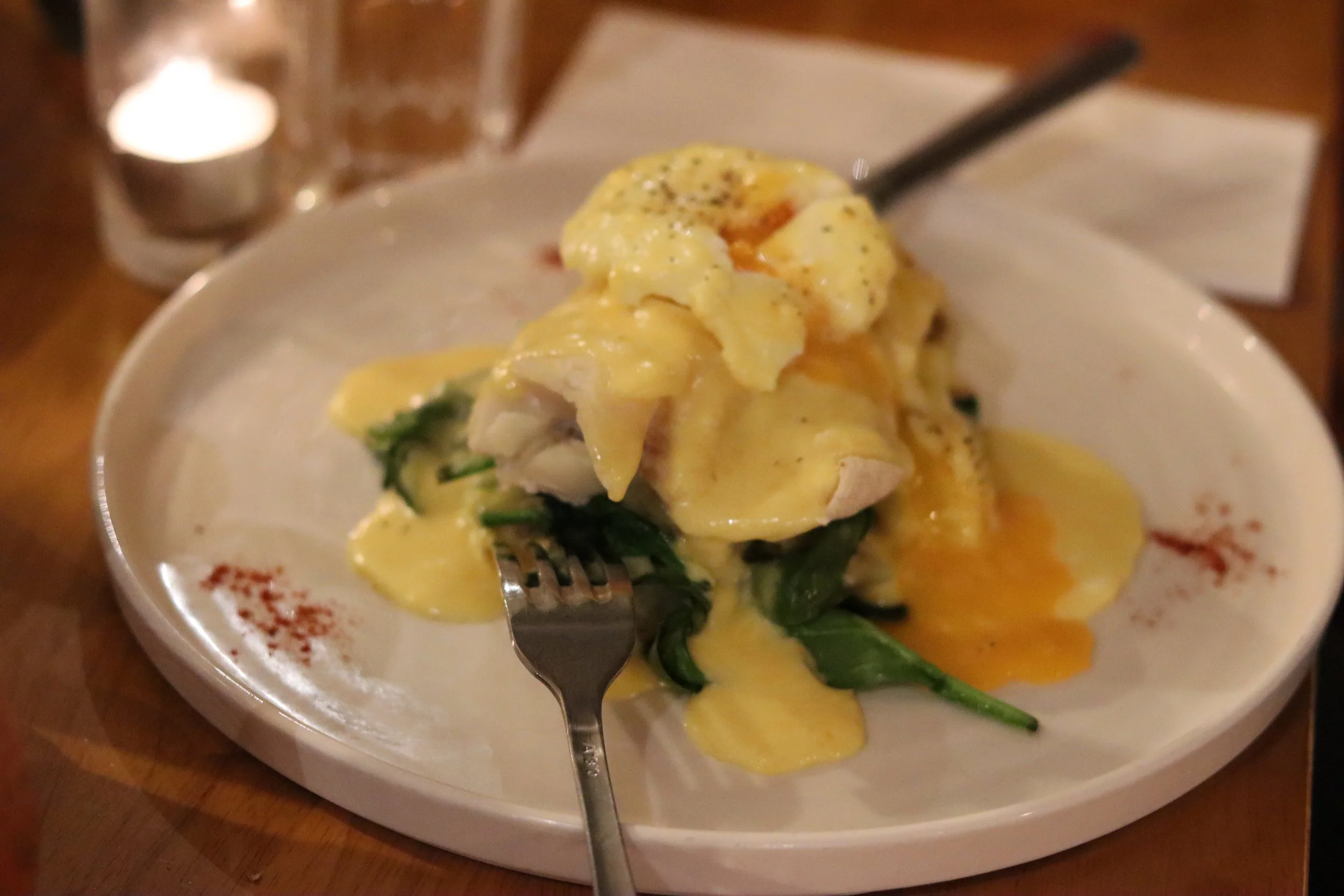 A plate of eggs benedict with hollandaise sauce, spinach, and possibly crab meat, on a white plate