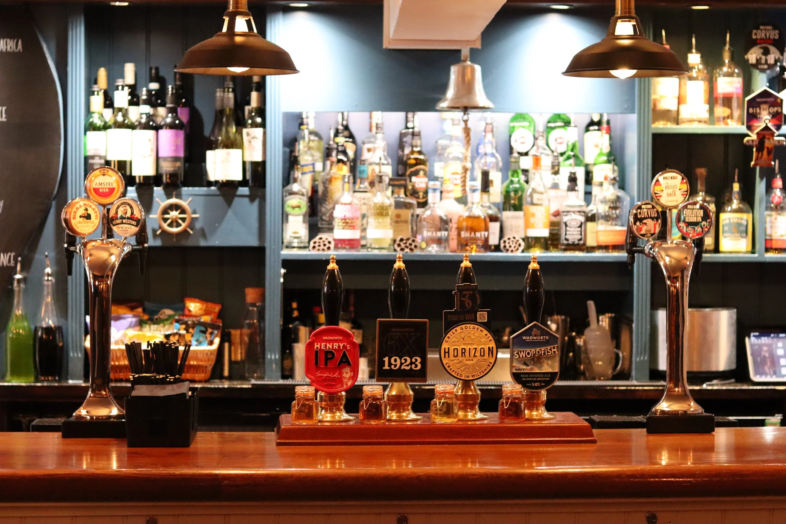 Bar counter with beer taps, bottles of alcohol on shelves, and small sample glasses for tasting