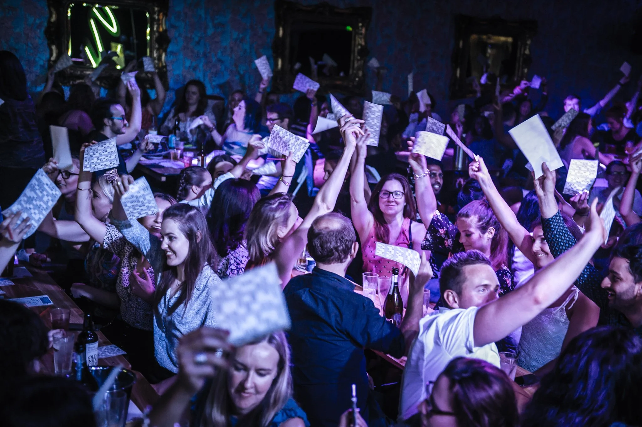 People at a lively bingo night in London event holding bingo cards and cheering.