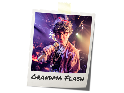 Grandma Flash from Hip Hop Bingo holding a microphone at a party or event, with colorful lights and a crowd in the background.