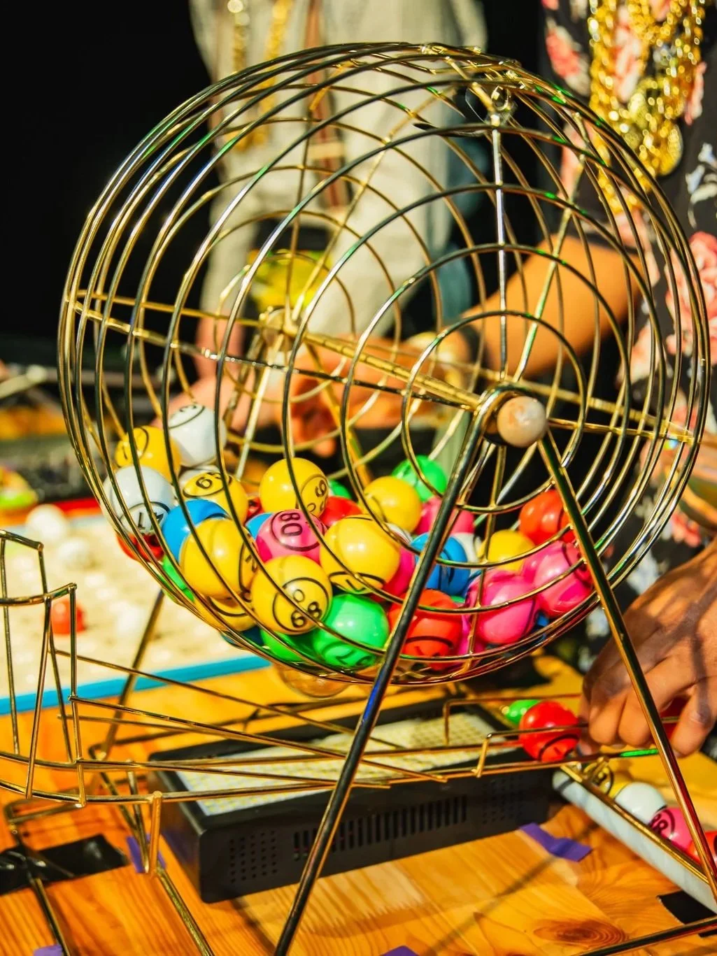 Colorful Bingo balls inside a metal cage, with a person pressing a button on a bingo machine.