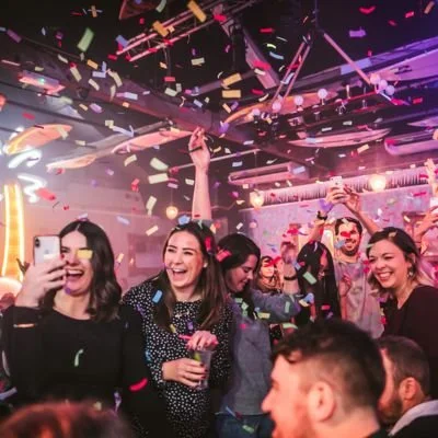 People celebrating at a party with colorful confetti falling, smiling, and taking photos.