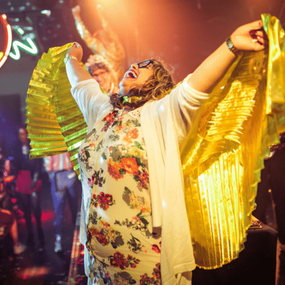 A woman joyfully winning bingo at Blingo event with yellow and gold flowing bingo wings at a lively event or party
