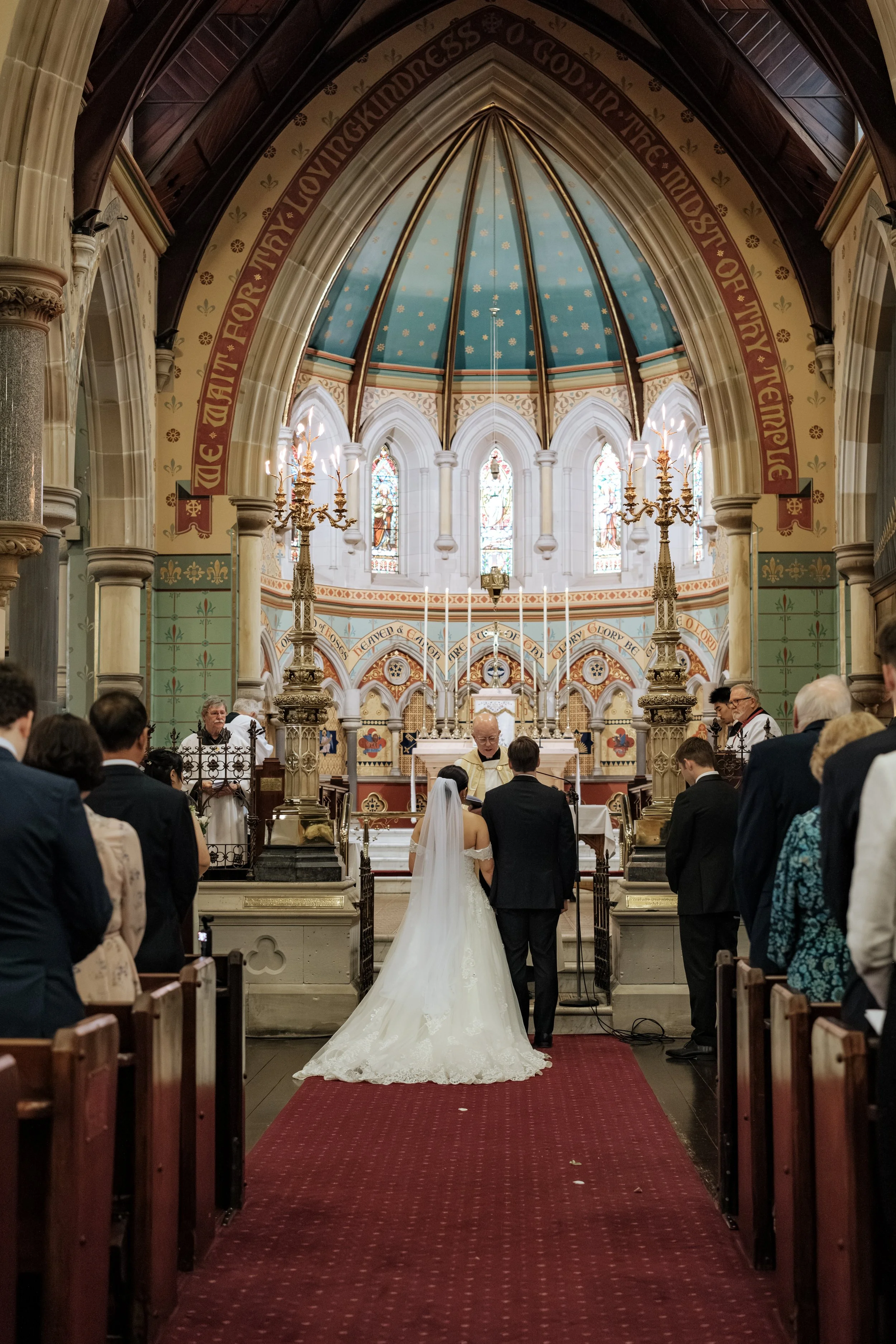 A wedding ceremony taking place inside a church with a bride and groom standing at the altar, surrounded by guests, during daytime.