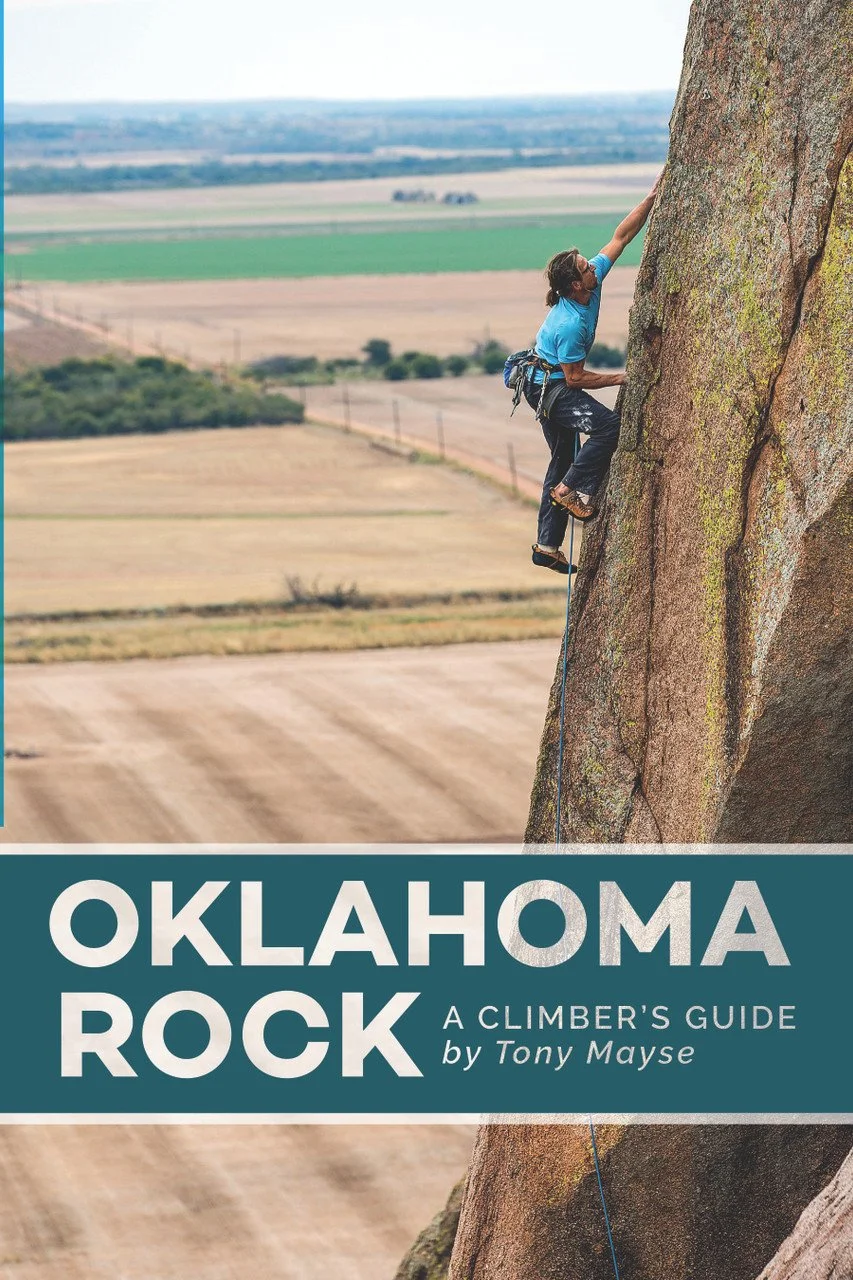 Climber ascending a large rock face with opens farmland and fields in the background