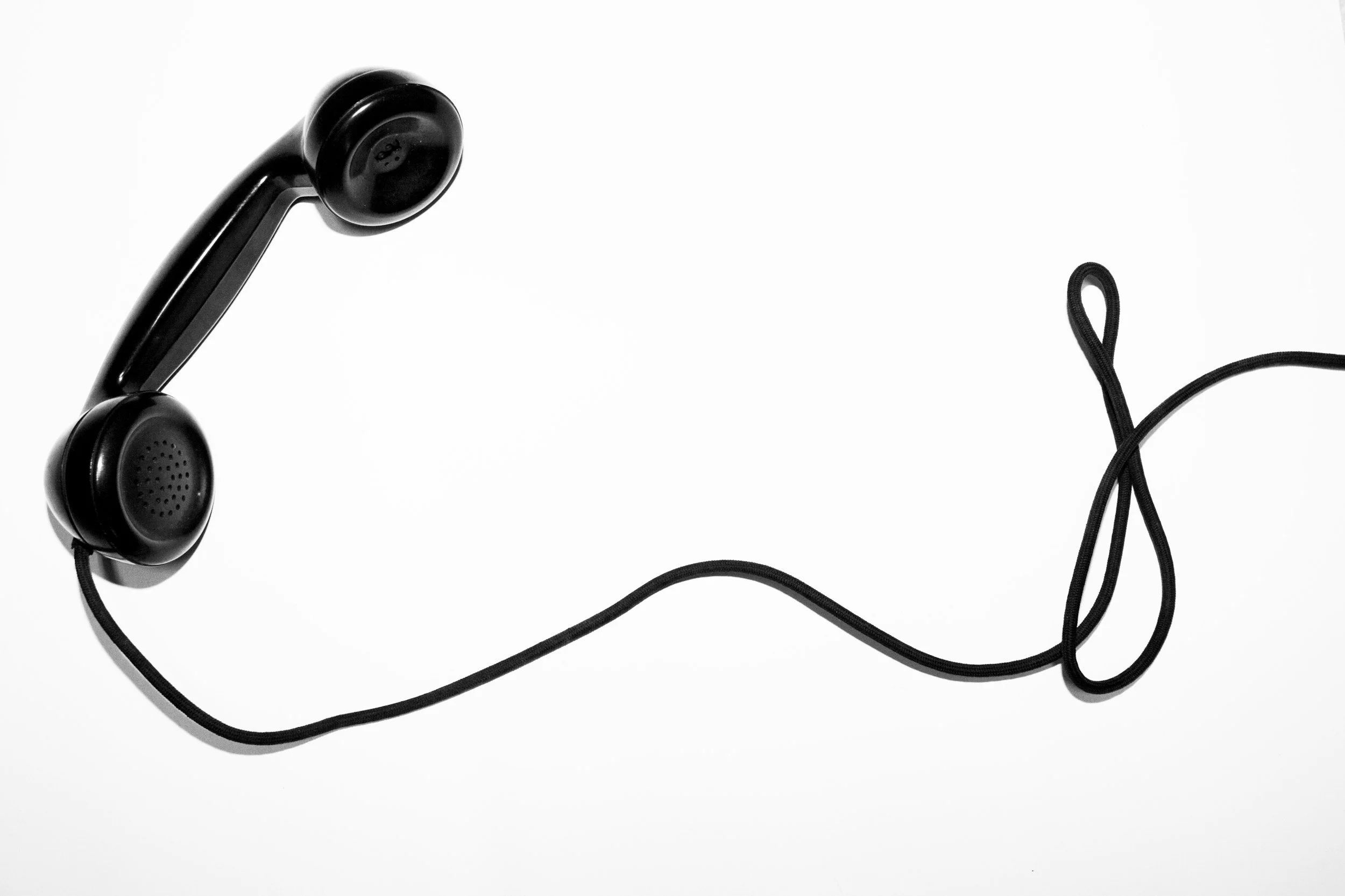 Black vintage telephone receiver with cord on white background.