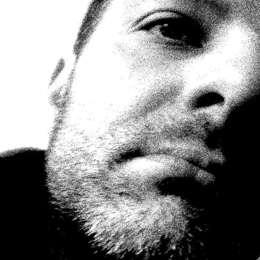 Close-up black-and-white, pixelated portrait of a person with a beard, eyes closed.