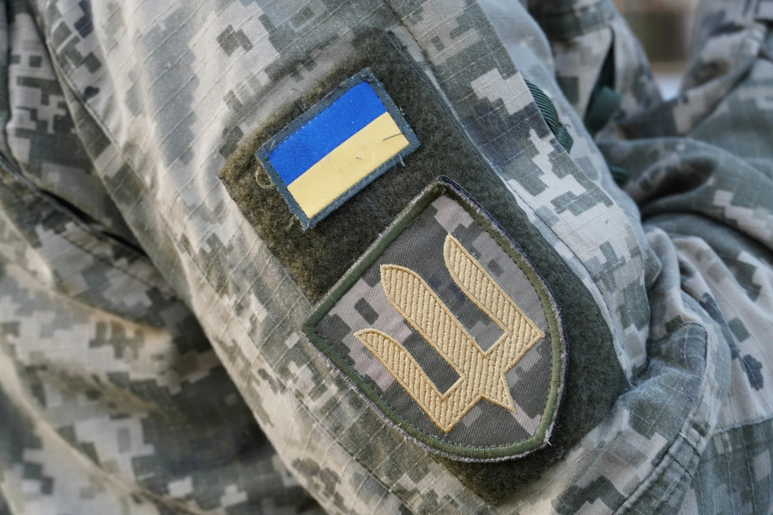 Close-up of a military uniform with patches, including the Ukrainian flag and a military rank insignia.