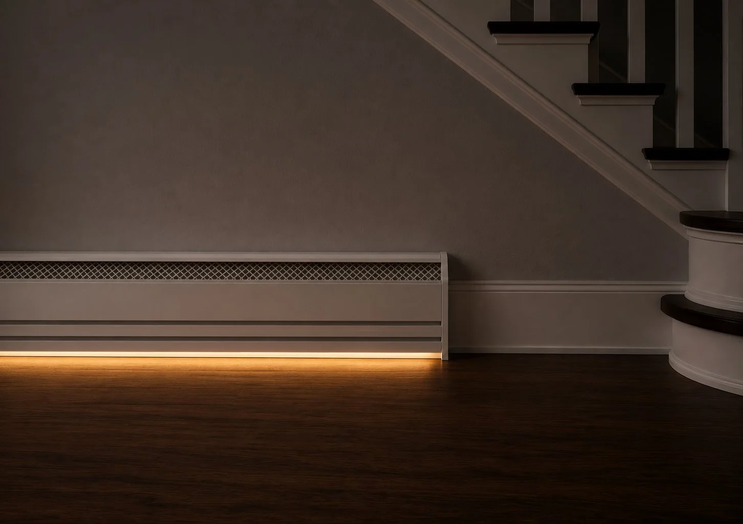 Interior of a home with a staircase on the right, a beige wall, and a white baseboard heater with LED lighting at the bottom, hardwood flooring, and a beige wall with decorative molding.