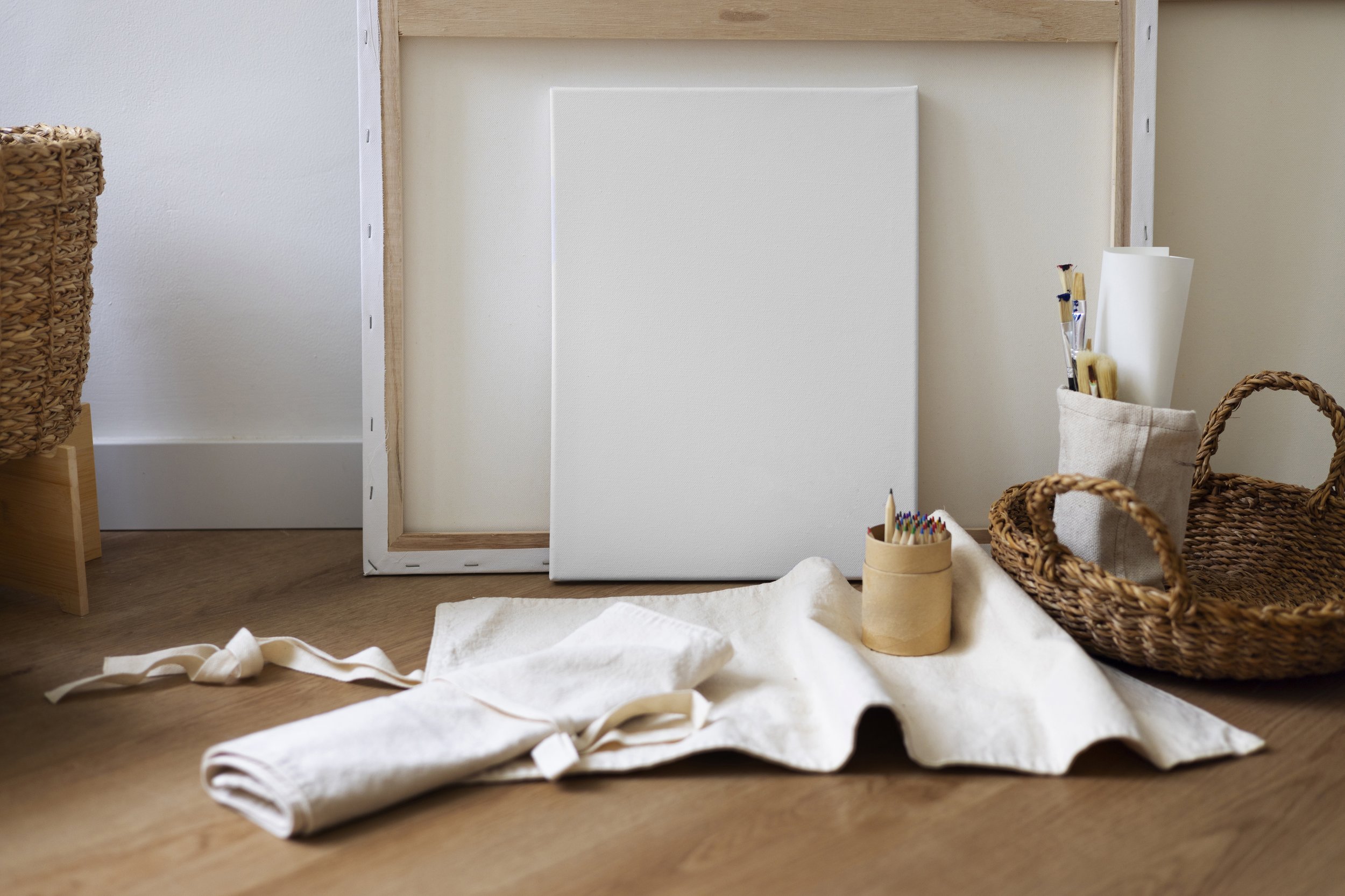 Art supplies and canvas in a cozy craft space with baskets and fabric on a wooden floor.