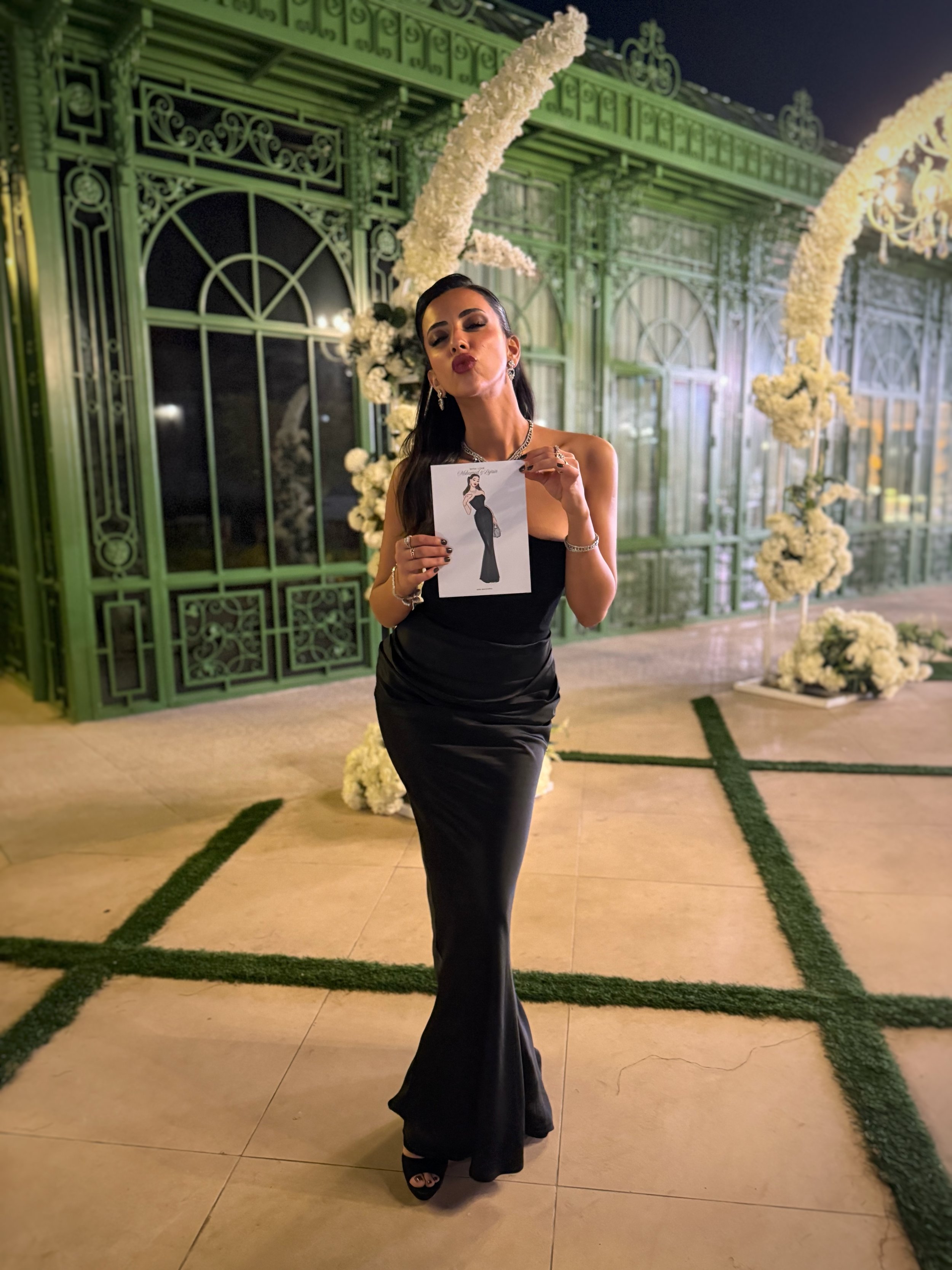 Woman in a black dress holding a card with a fashion illustration created during wedding or event