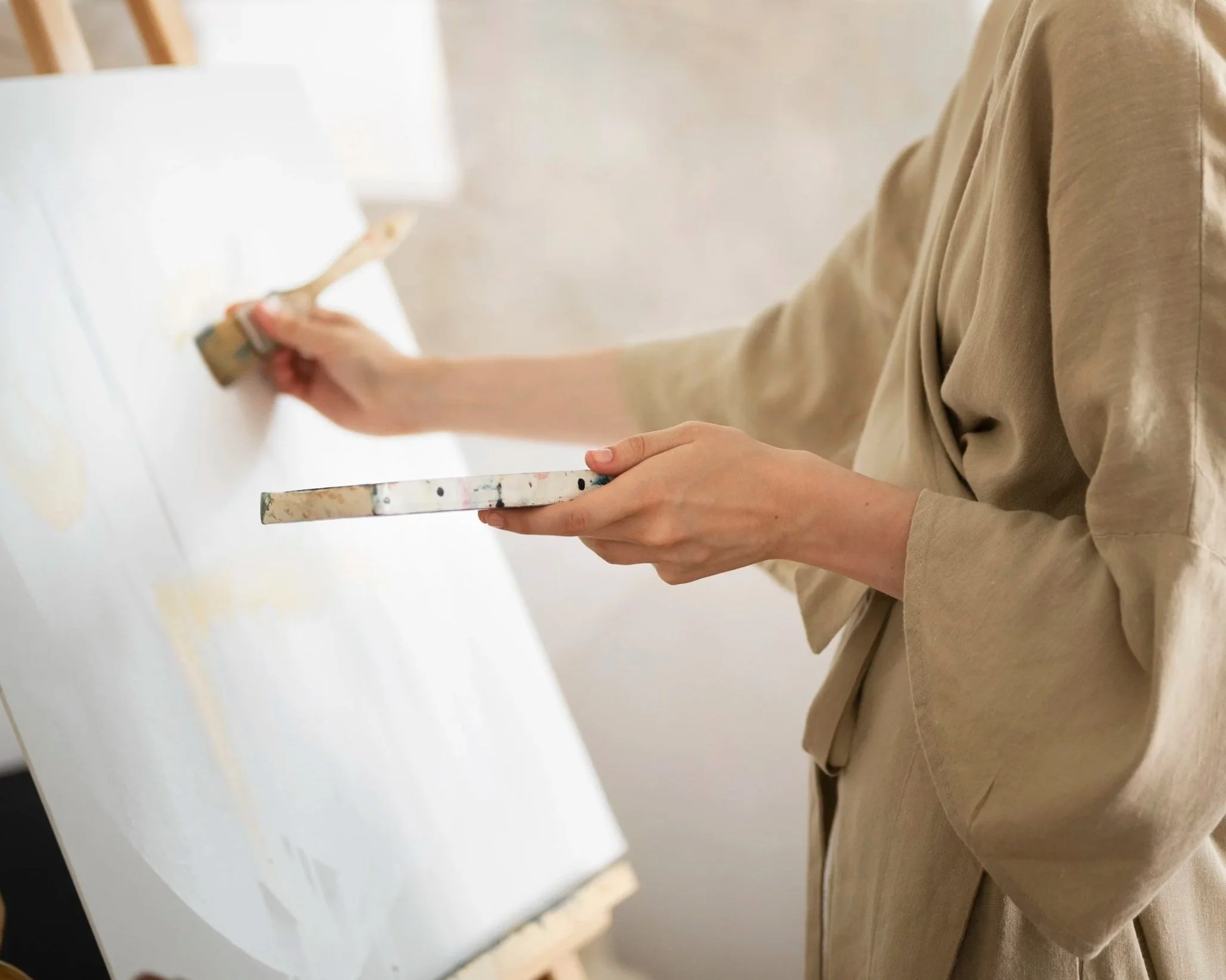 Person painting a wall with a paintbrush, wearing a beige shirt.