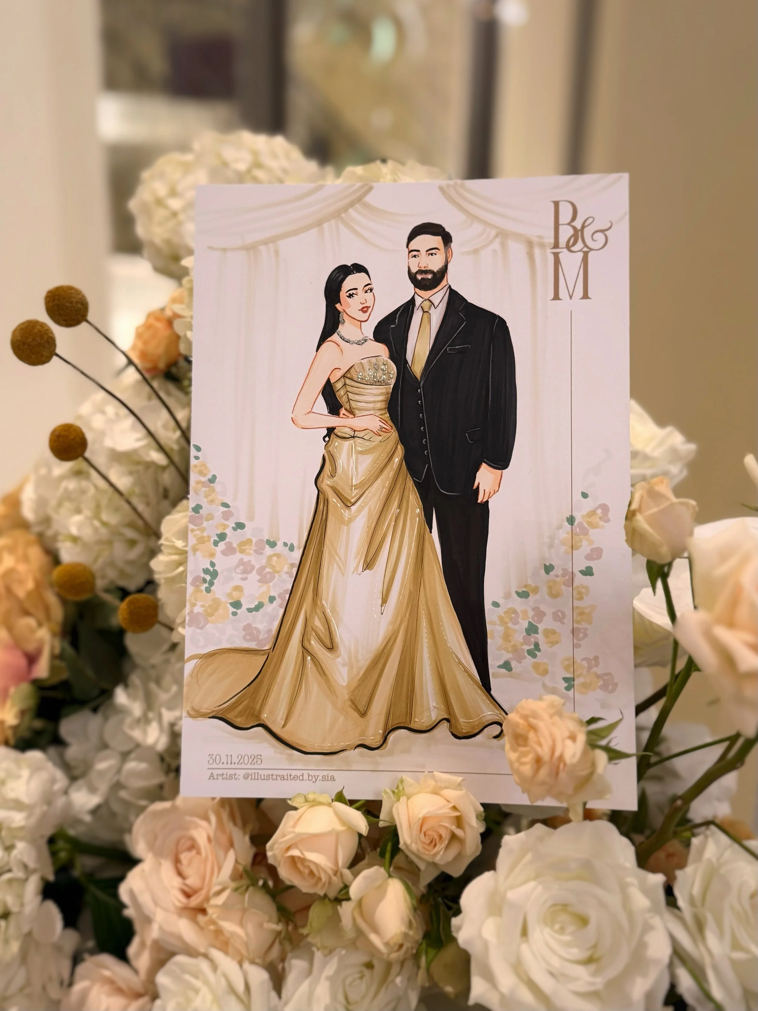 Illustration of a bride and groom standing together, with the bride wearing a gold gown and the groom wearing a black suit. The illustration is set against a backdrop of white drapery. The image is surrounded by a floral arrangement of white and pale
