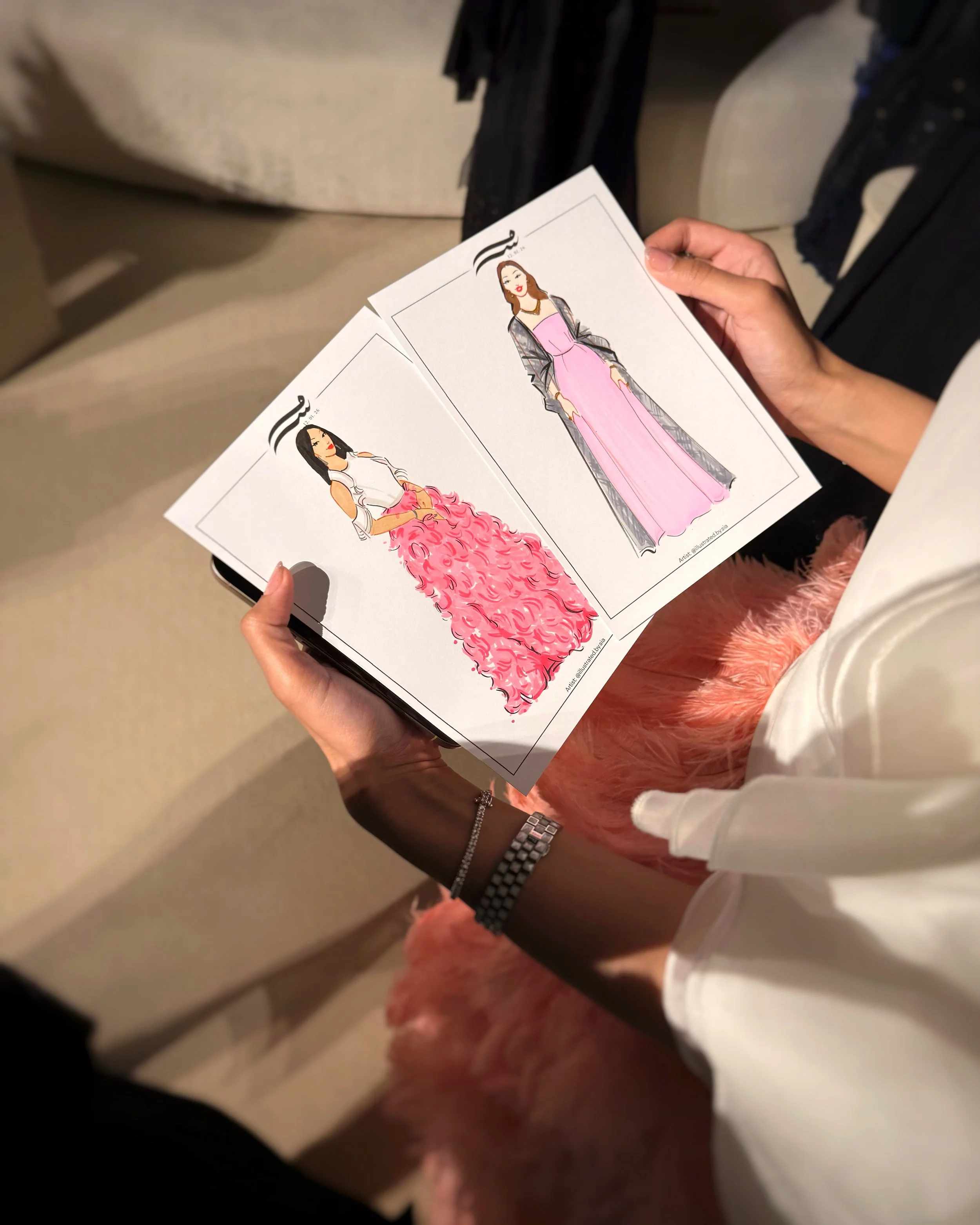 Person holding two fashion sketches of women in elegant dresses 