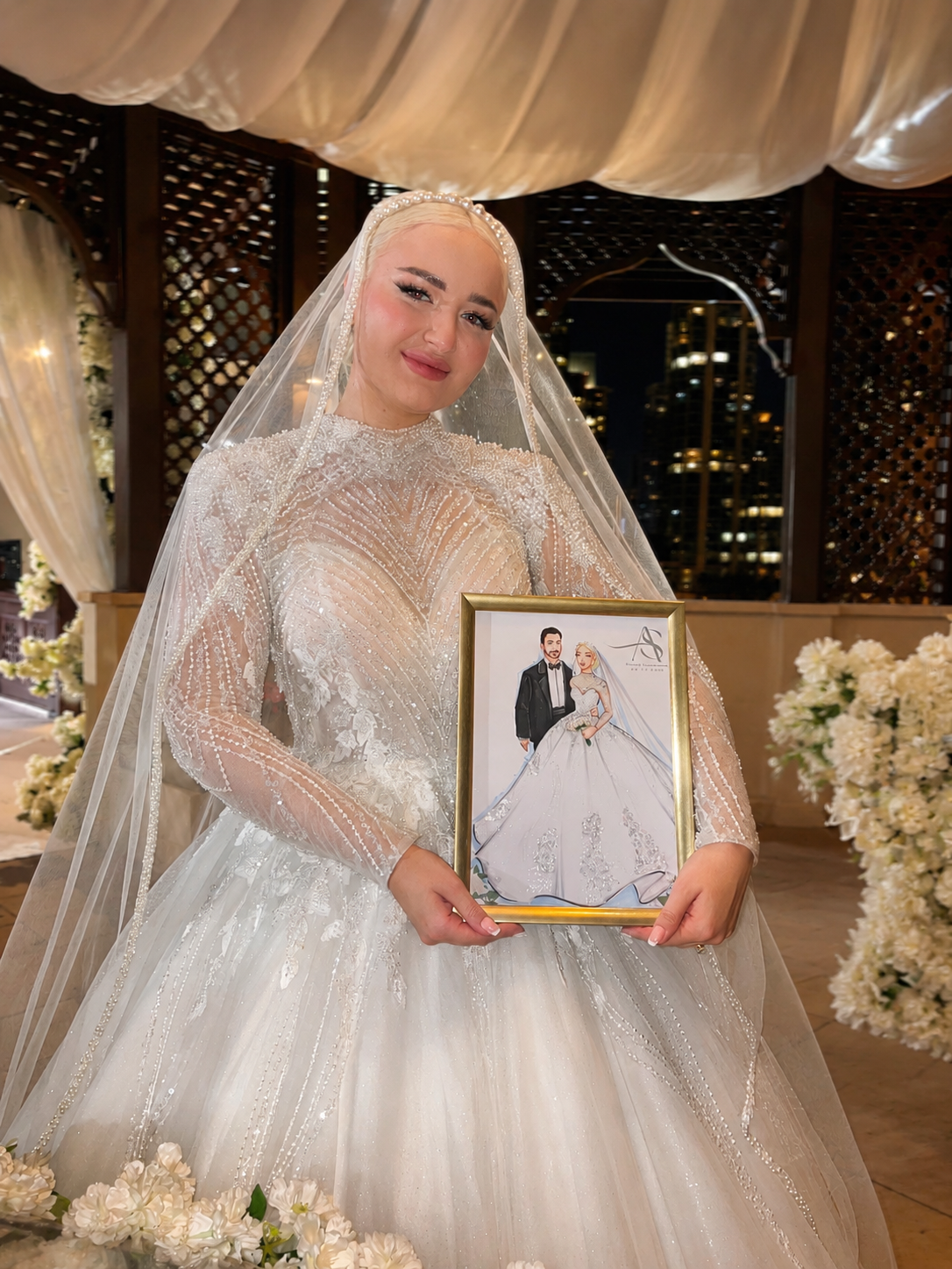 A bride in a wedding gown and veil holding a framed portrait of herself and her groom at a wedding reception.