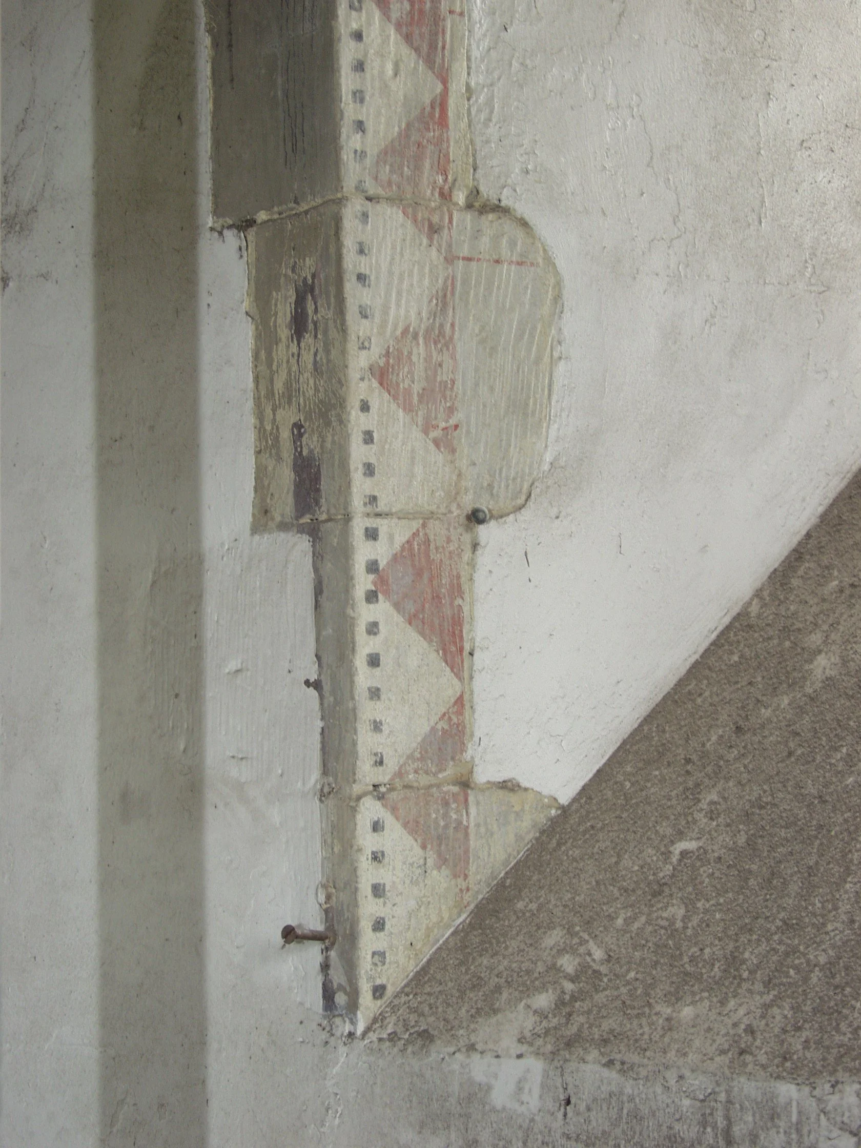 Close-up of a corner of a wall with old paint and plaster, showing a partially removed or damaged section revealing underlying construction material and markings.