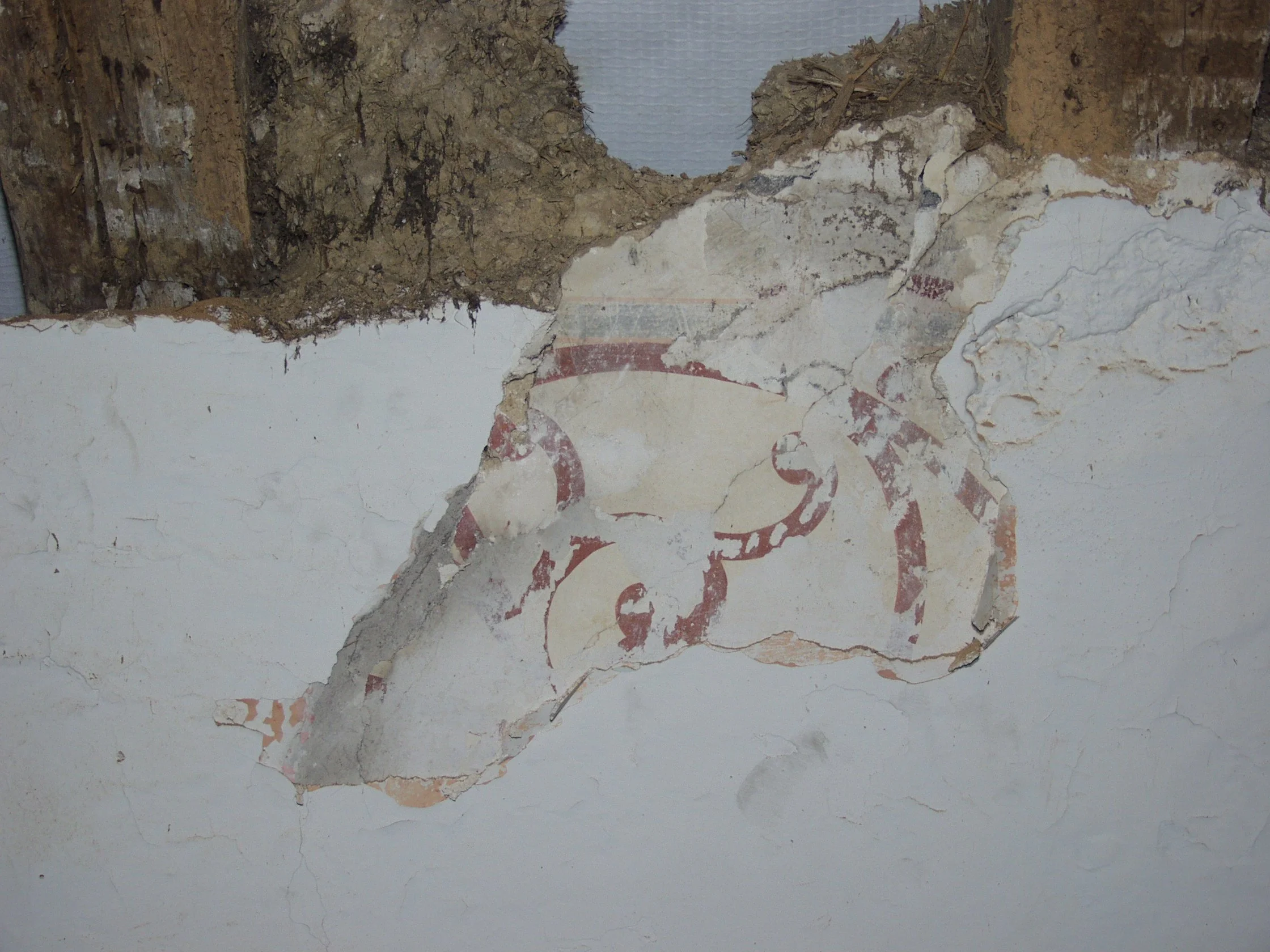 Deteriorating wall with peeling paint, exposed plaster, and crumbling corner with visible dirt and debris.