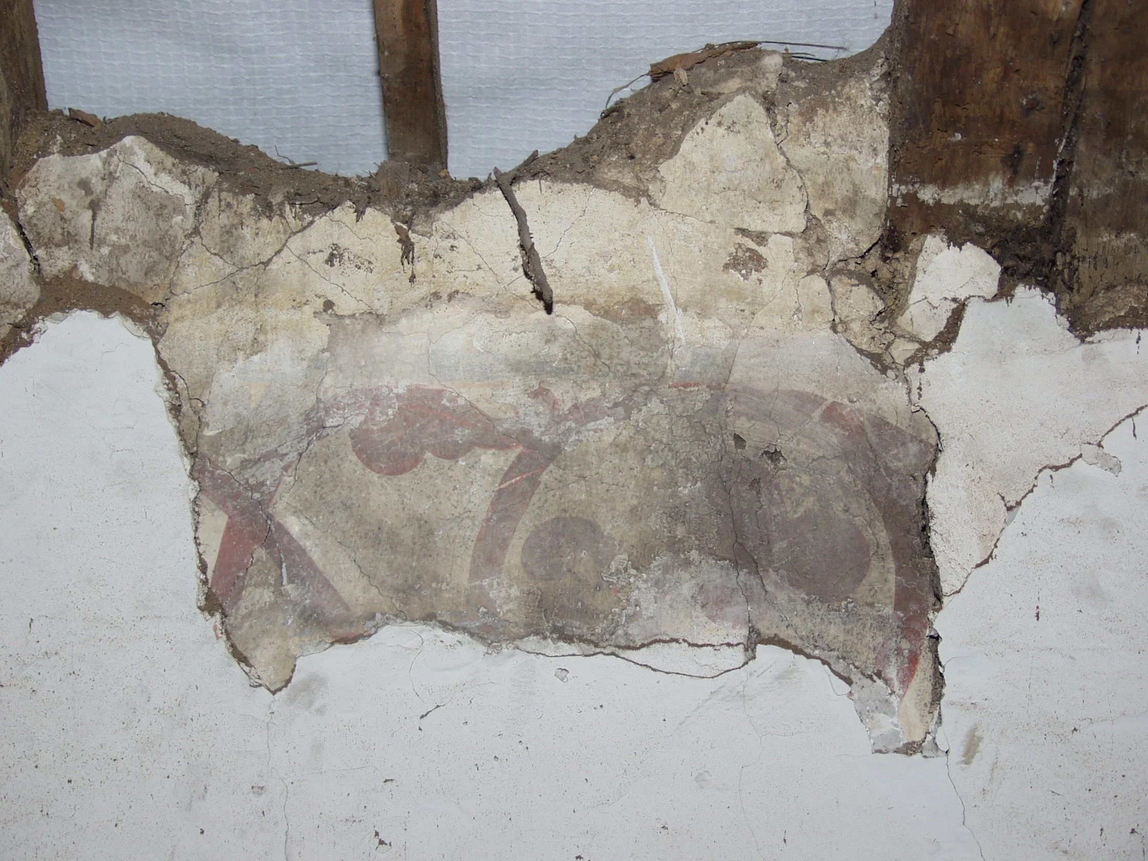 Broken wall with exposed bricks and a worn-down painted surface featuring a faded, partially visible logo or design.