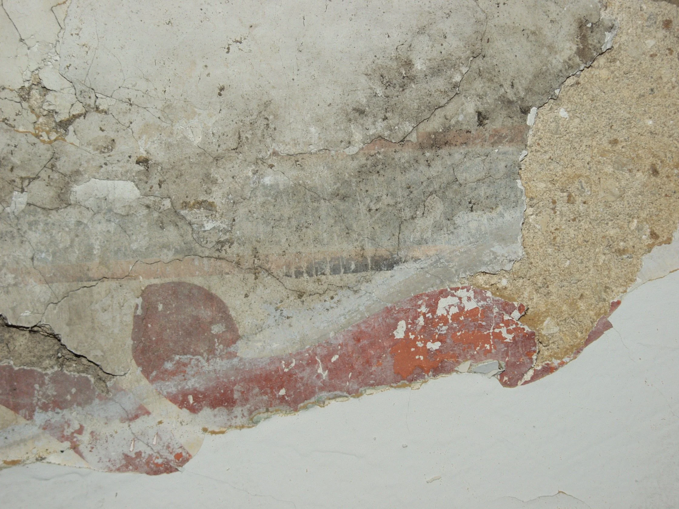 Close-up of a damaged and peeling section of an old painted wall showing layers of paint and plaster with cracks and discoloration.