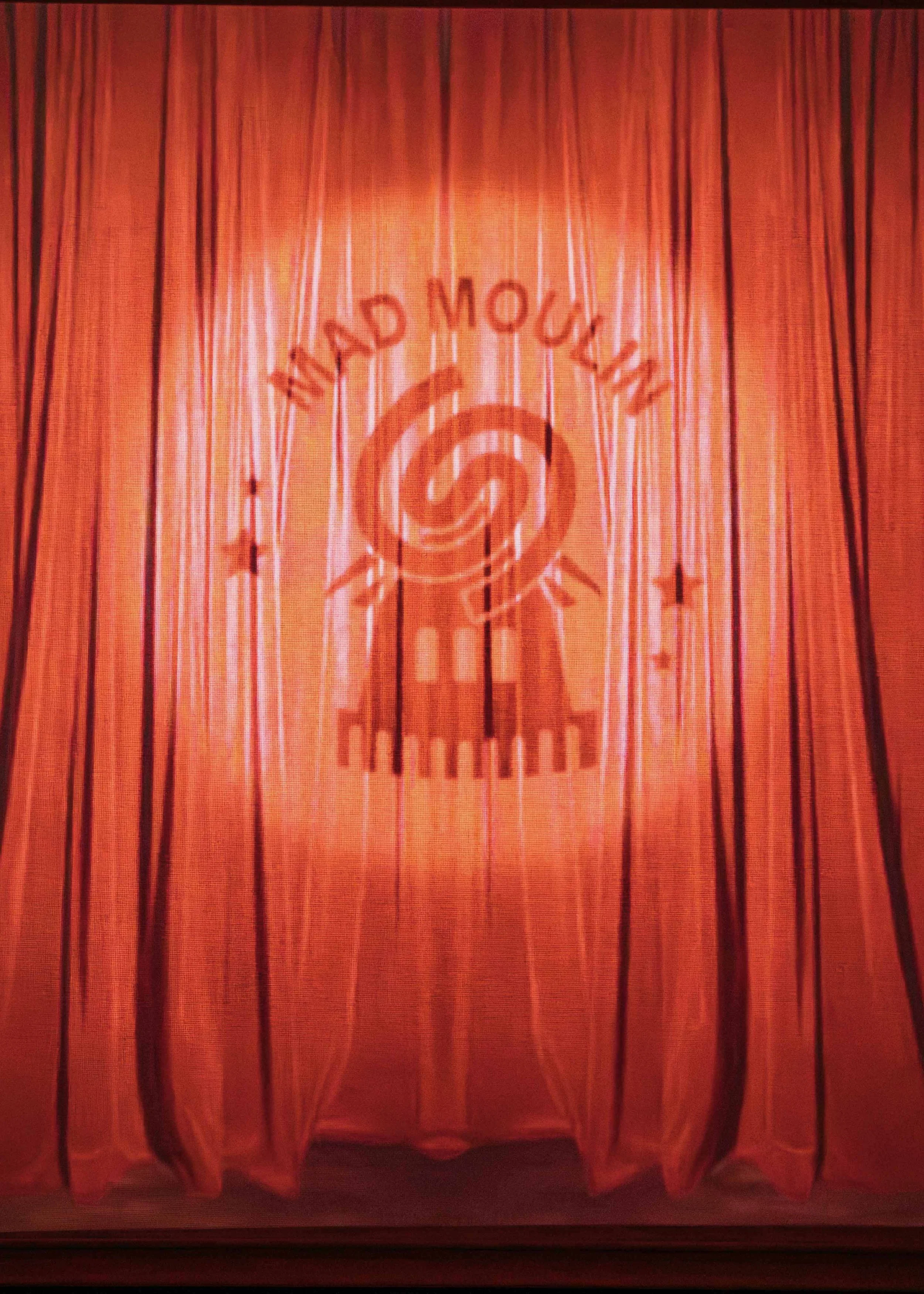 A red stage curtain with the words "Mid Mind Moving" and a logo of a spiral with a lighthouse and two stars.