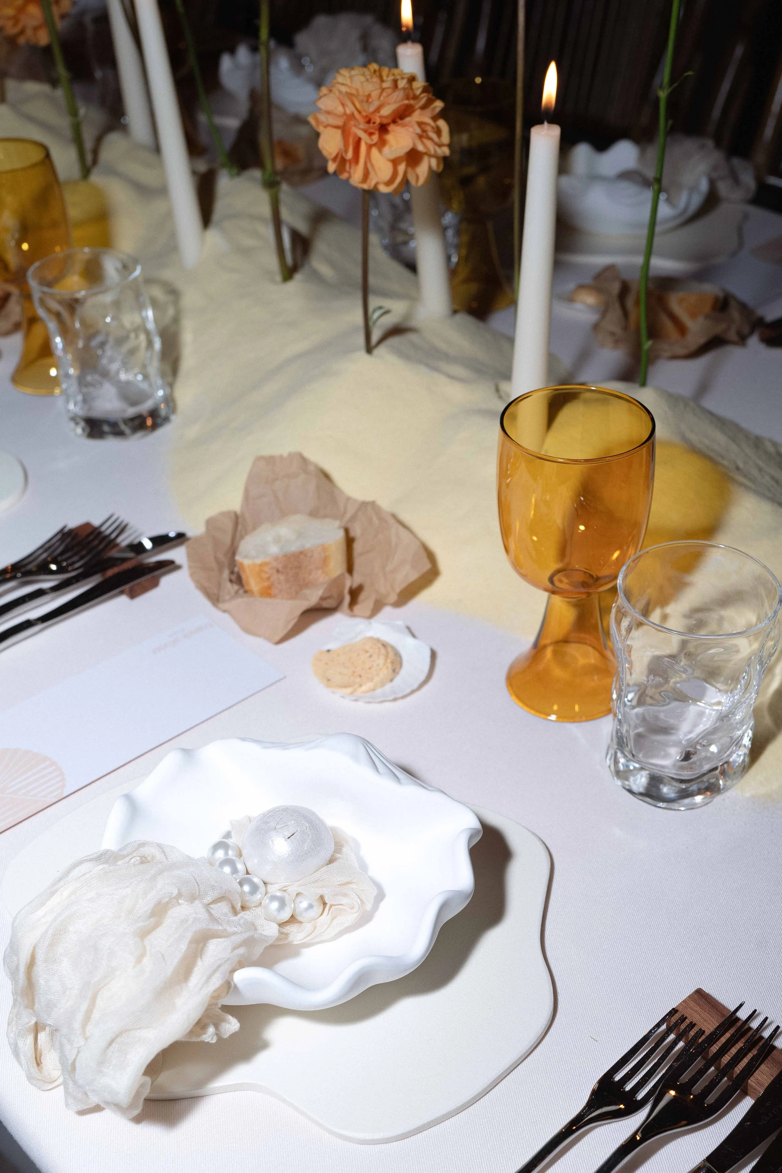Decorated dining table with candles, flowers, wine glass, water glasses, bread, and a centerpiece with candles and flowers.