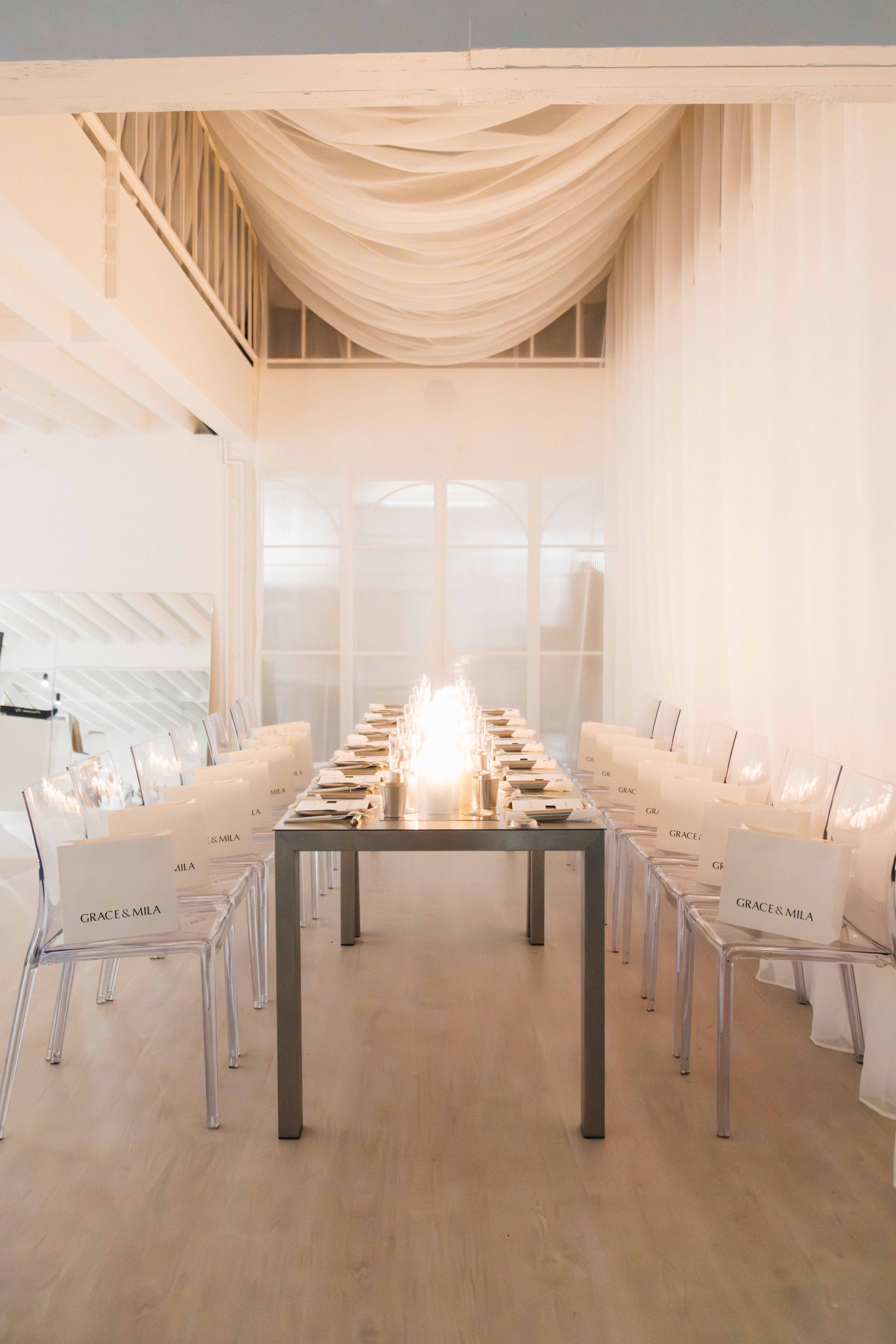 Elegant dining table setup with white chairs and window in the background, featuring personalized signs with names 'Grace & Mila'.