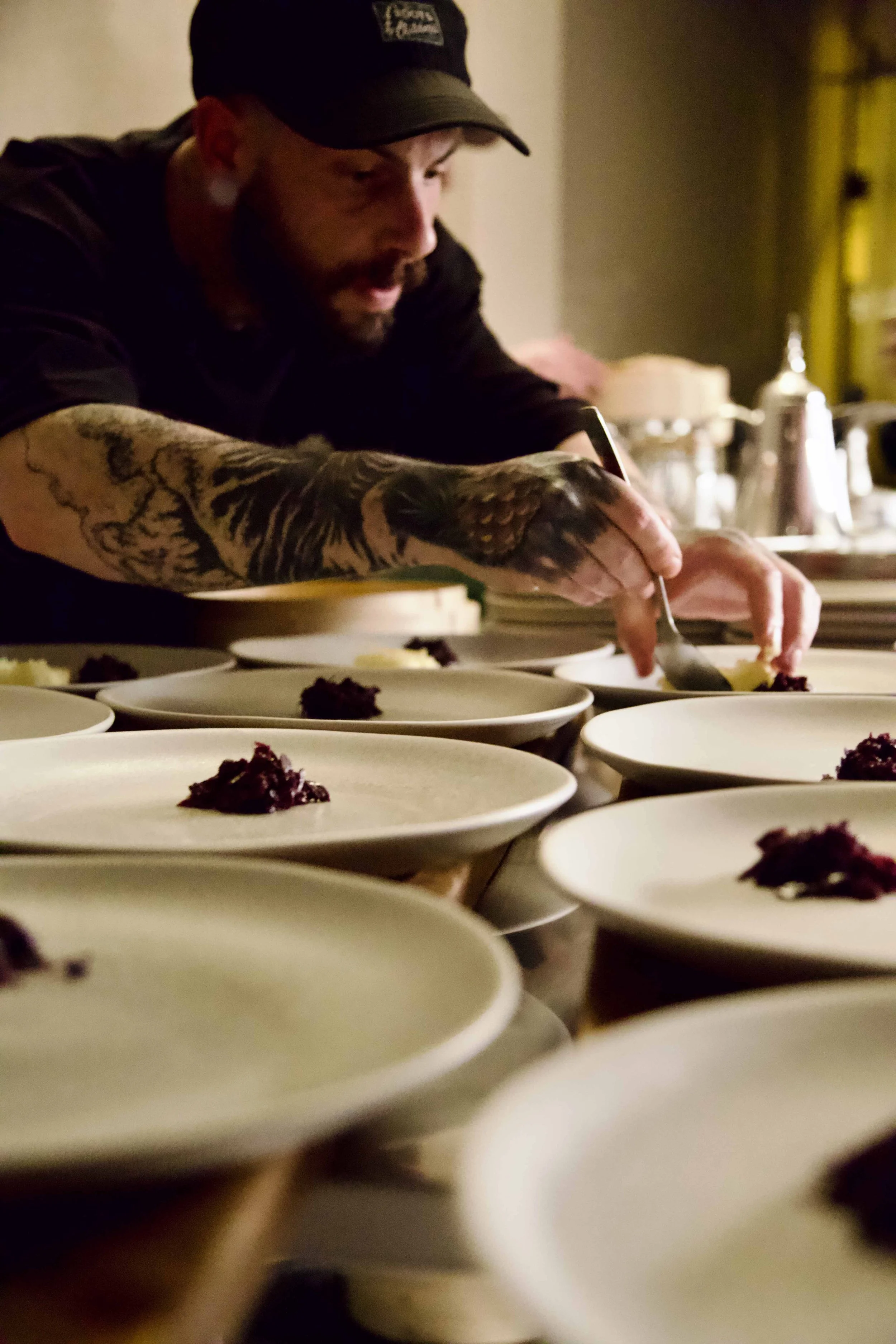 A tattooed chef is placing food on white plates in a kitchen.
