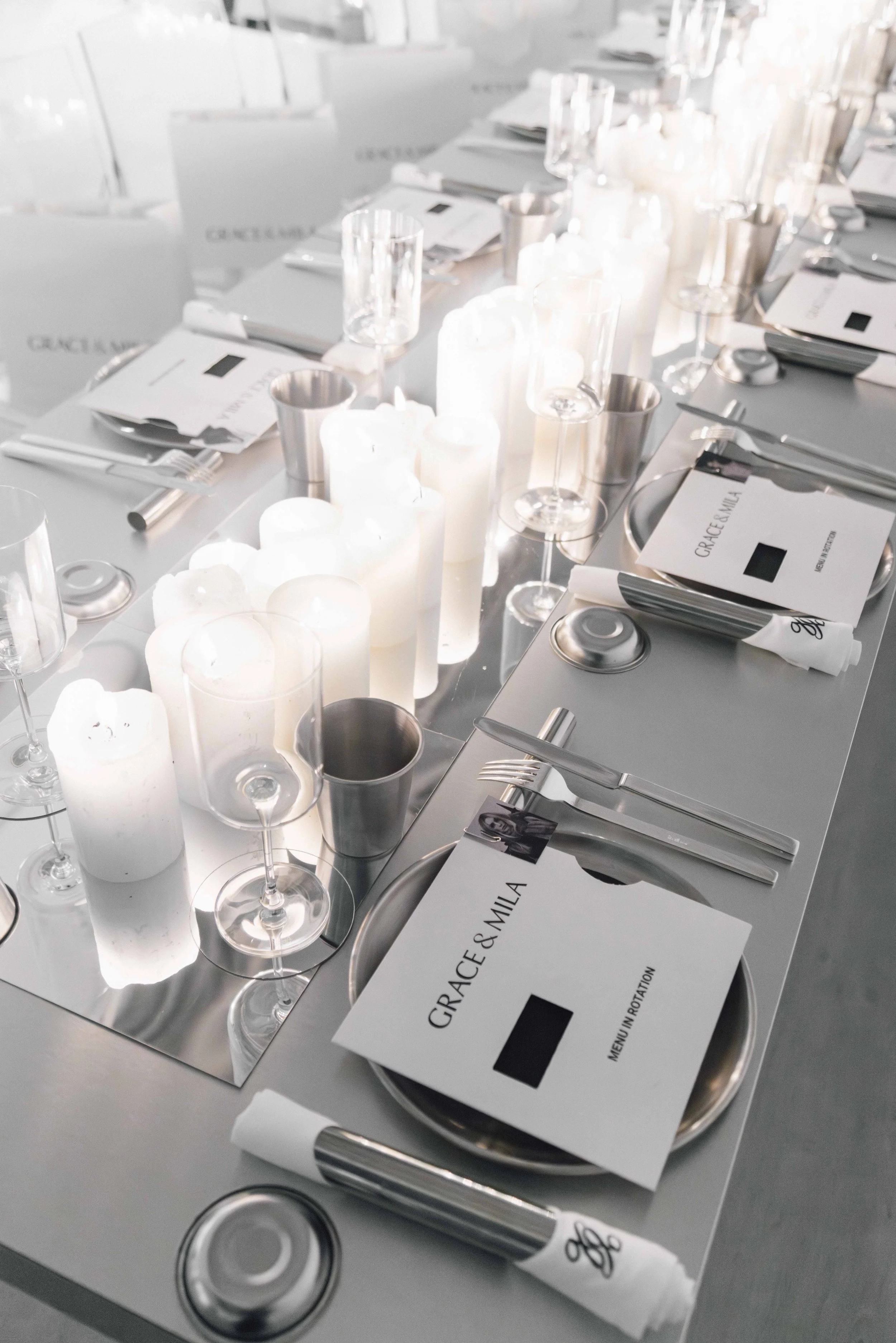 Elegant table setting with white candles, glasses, silverware, and menus for an event or wedding reception.