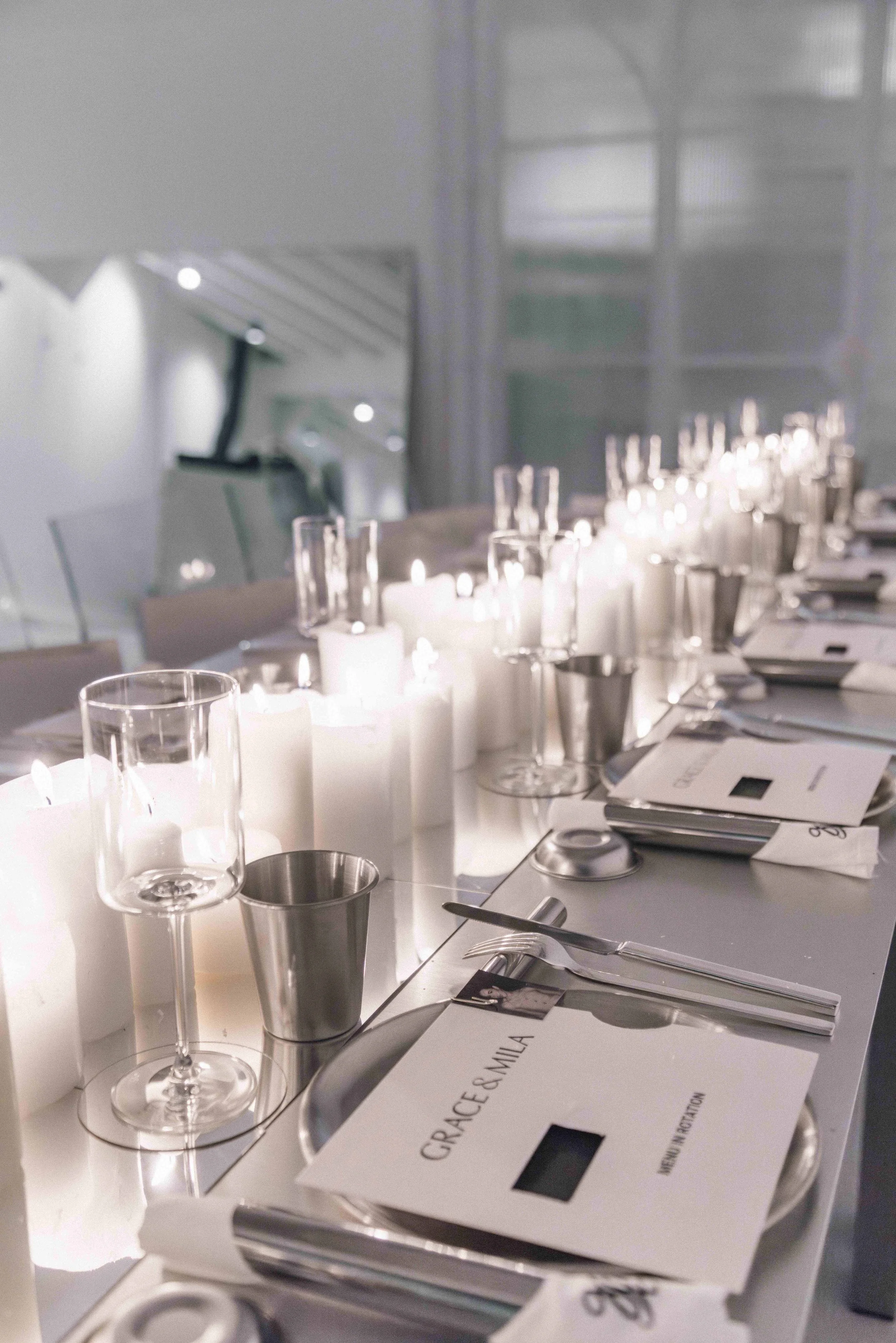Elegant dining table set with white candles, empty wine glasses, and silverware, ready for a formal event.