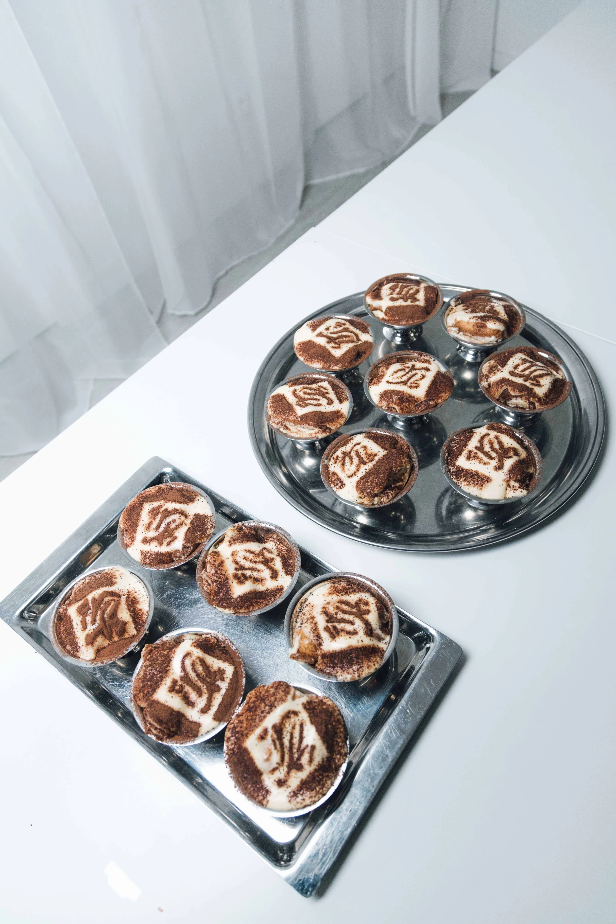 Dessert cups with a logo on top, placed on a silver tray and a round silver platter.