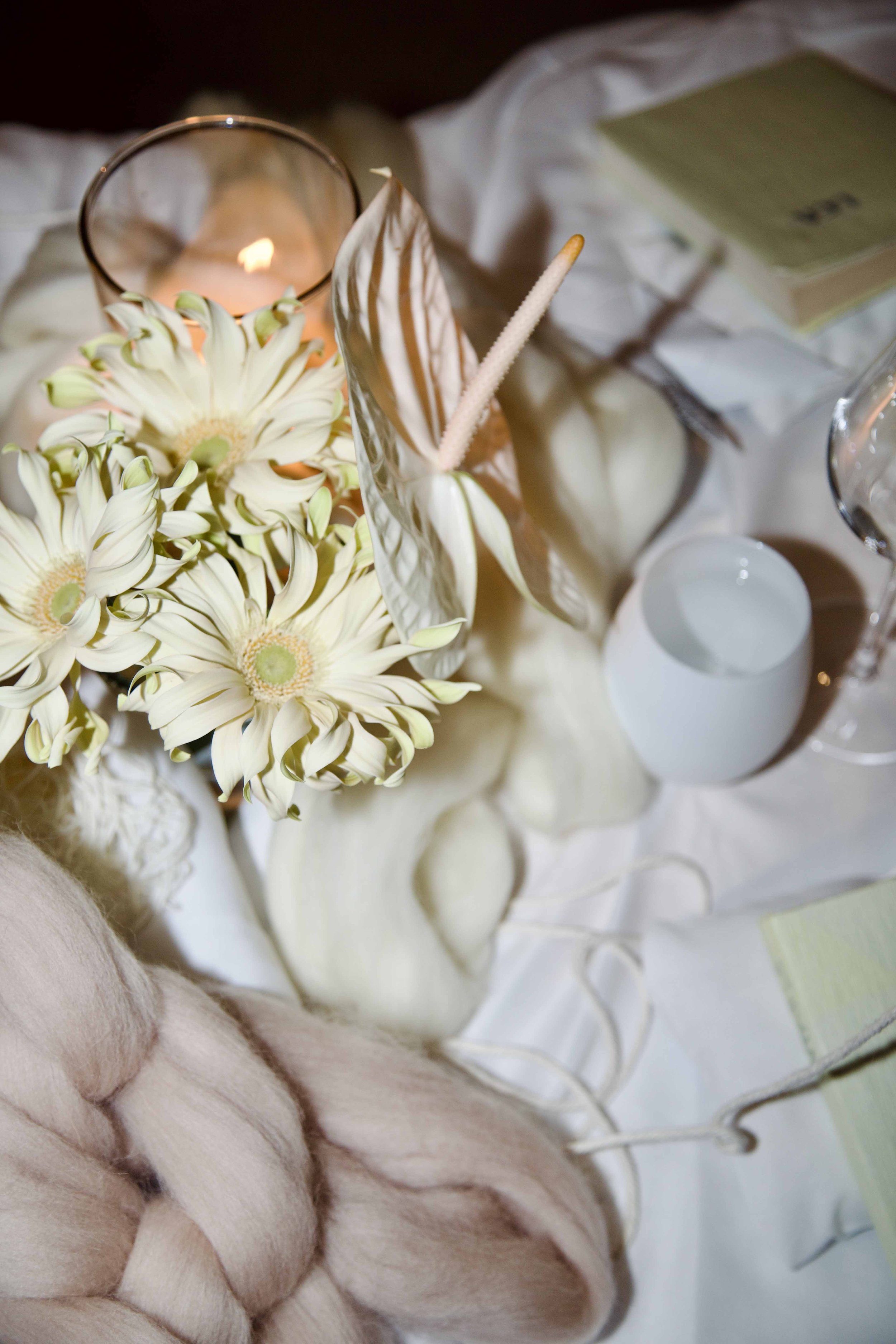 Close-up of a table centerpiece with white flowers, candles, and decorative items on a white cloth table.