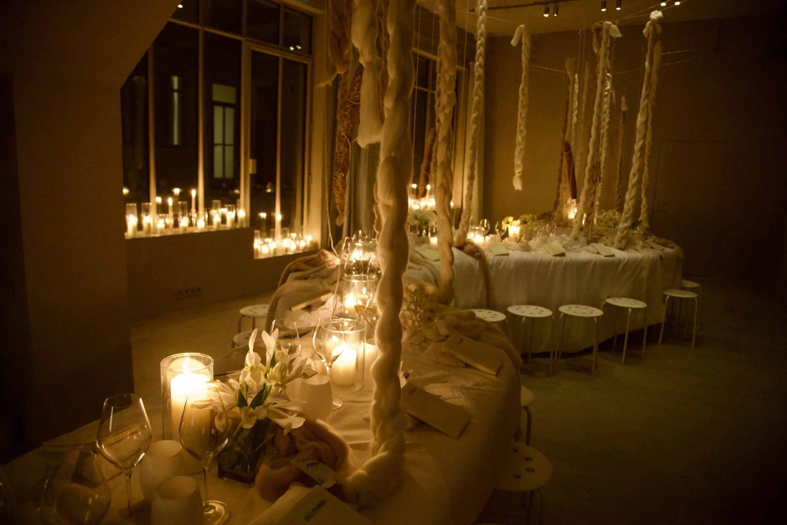 Dimly lit interior with long tables decorated with candles, flowers, and twisted fabric hanging from the ceiling, creating a warm, intimate atmosphere.