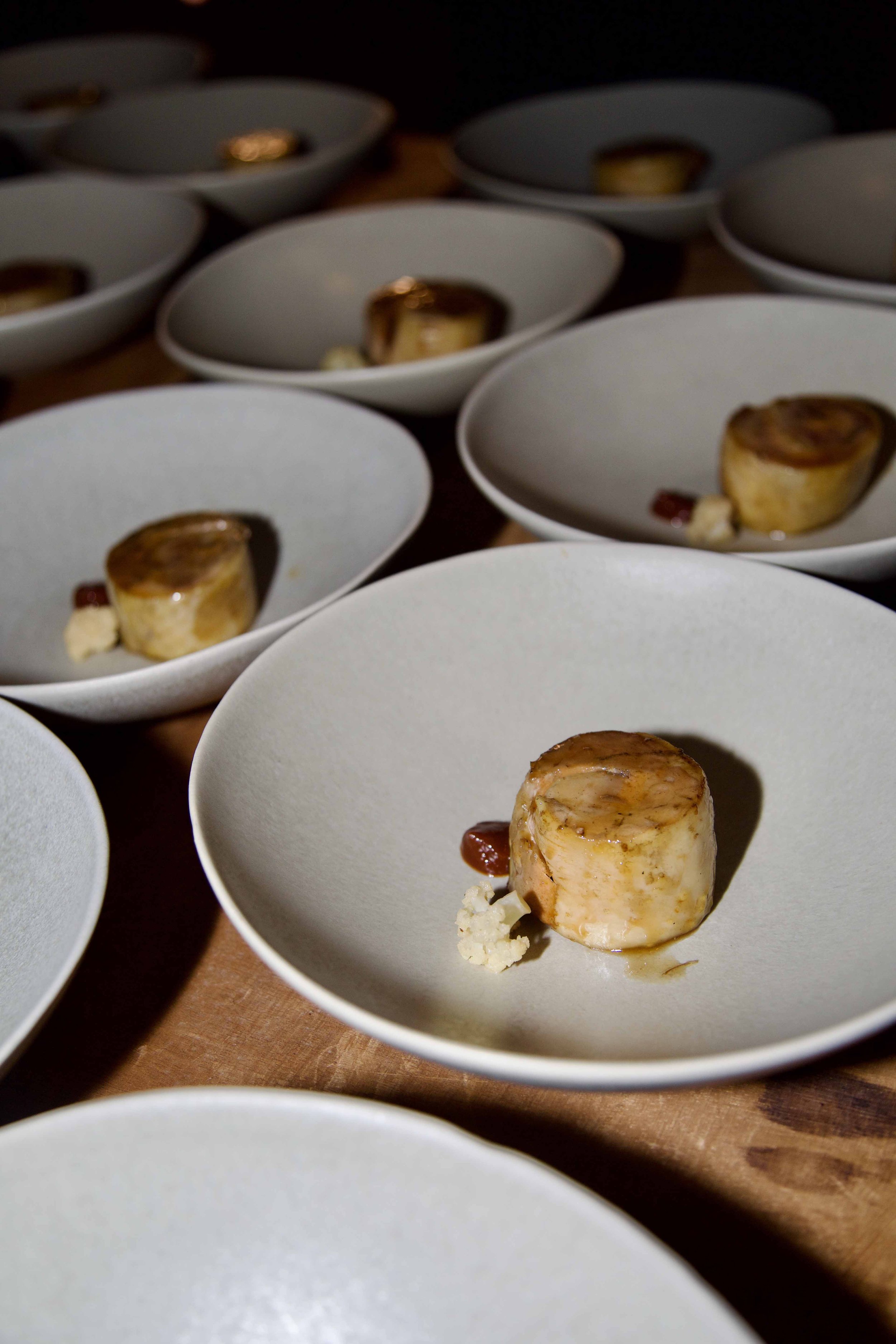 Multiple white plates with individual servings of a small, round, baked dish topped with sauce and garnished with small bits of cheese.