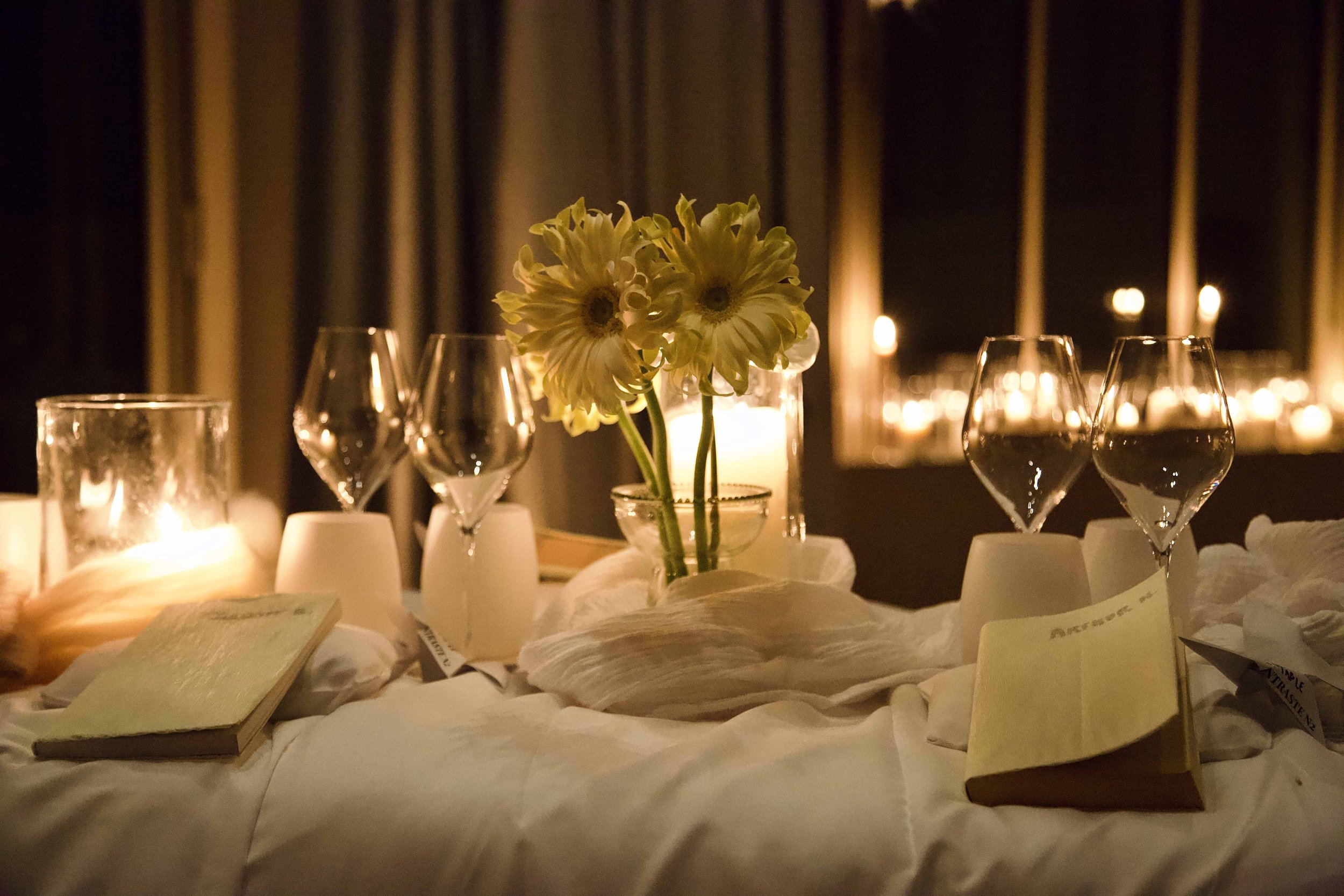 A cozy table setting with yellow flowers in a glass vase, four wine glasses, and candles creating a warm ambiance.