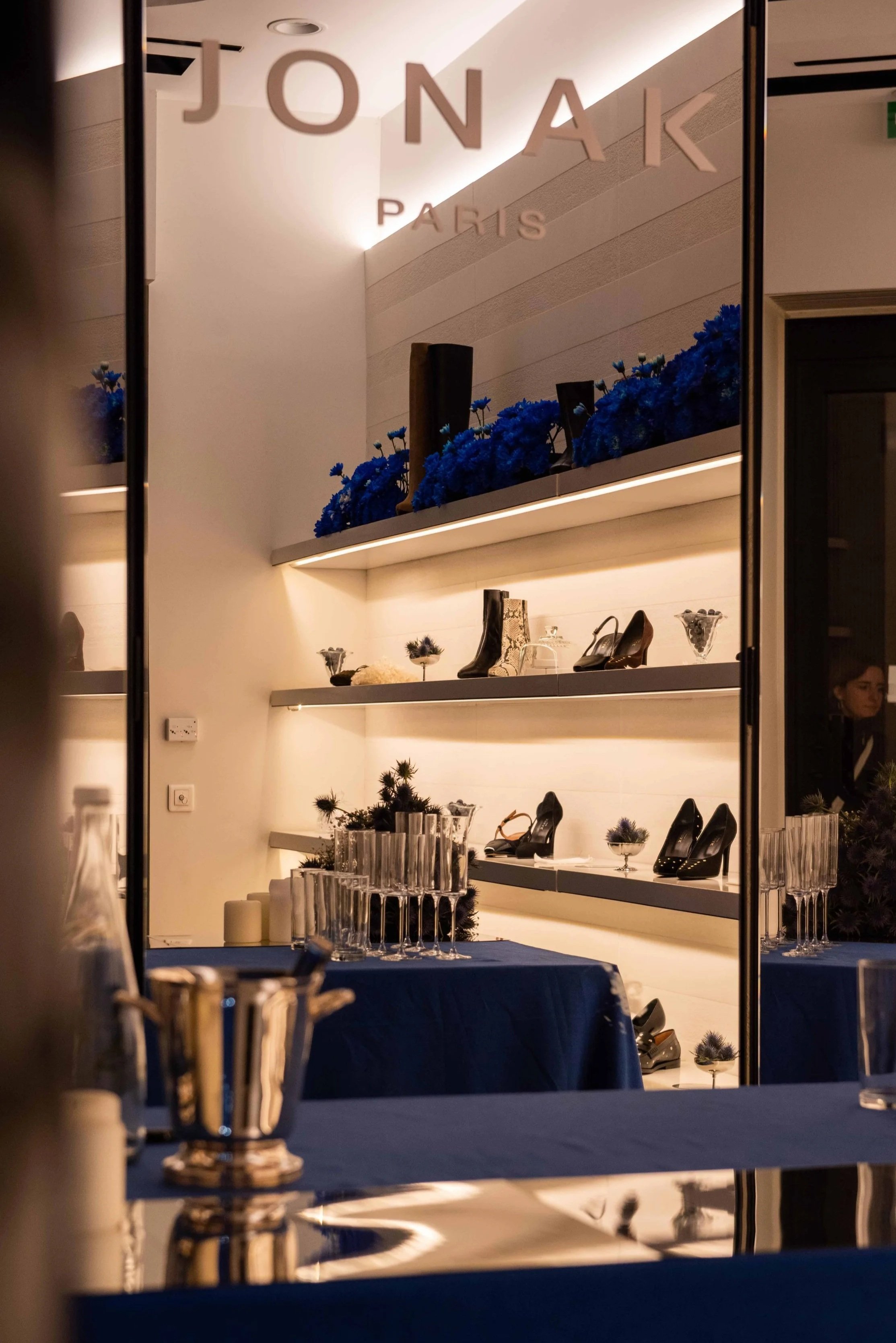 Display shelf with shoes and decorative items, blue flowers on top, with a sign reading 'JONA K PARIS' above.