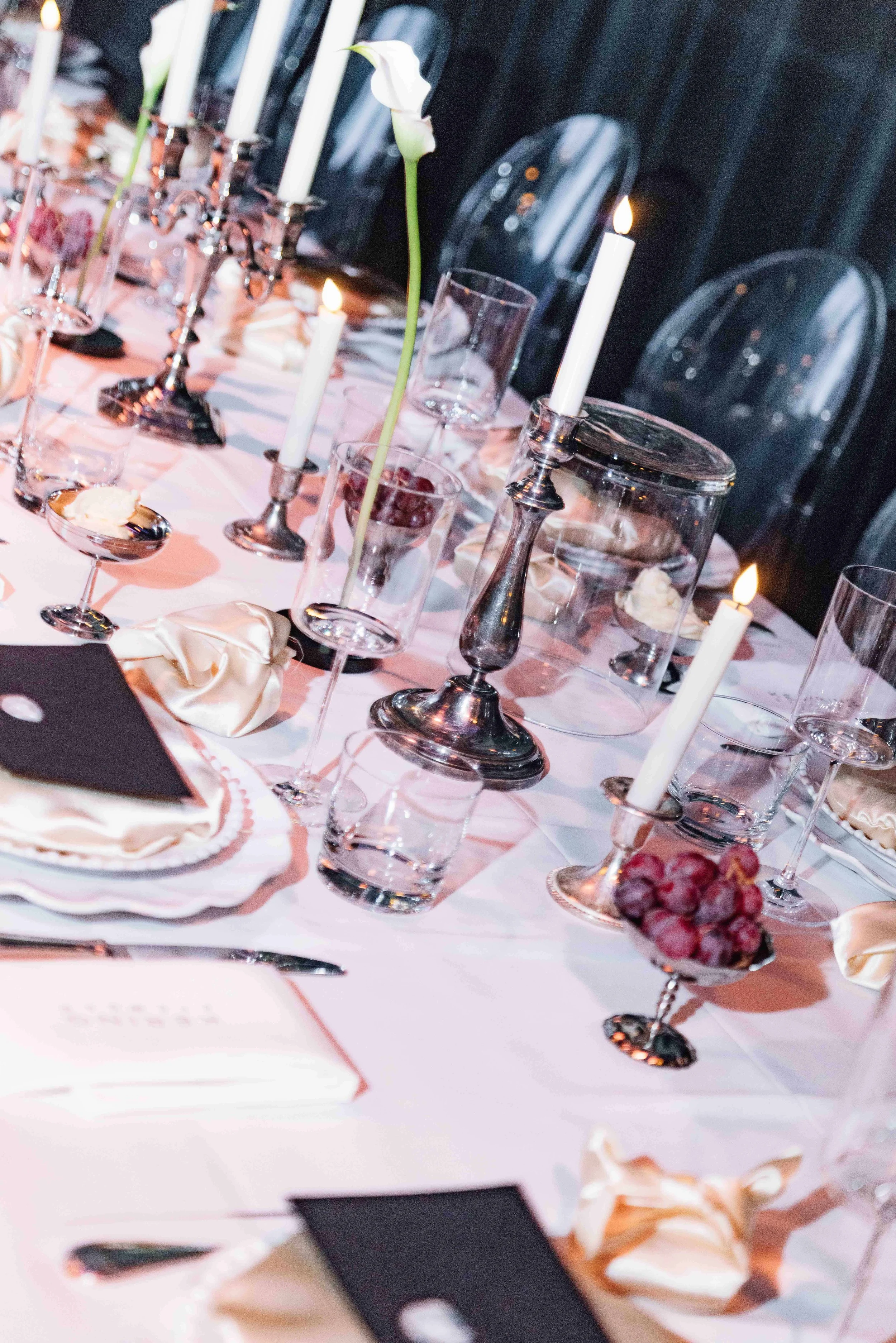 Elegant dining table with lit candles, glassware, a decorative flower, and place settings for a formal event.