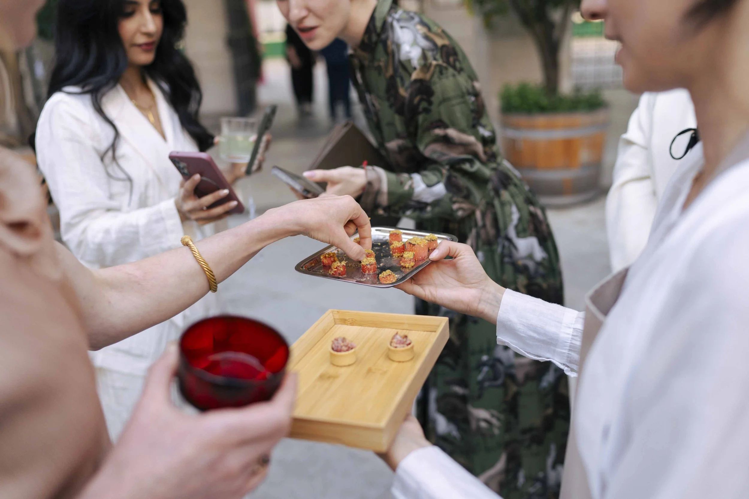 People at an outdoor gathering sharing food, including sushi, with some holding drinks and phones.