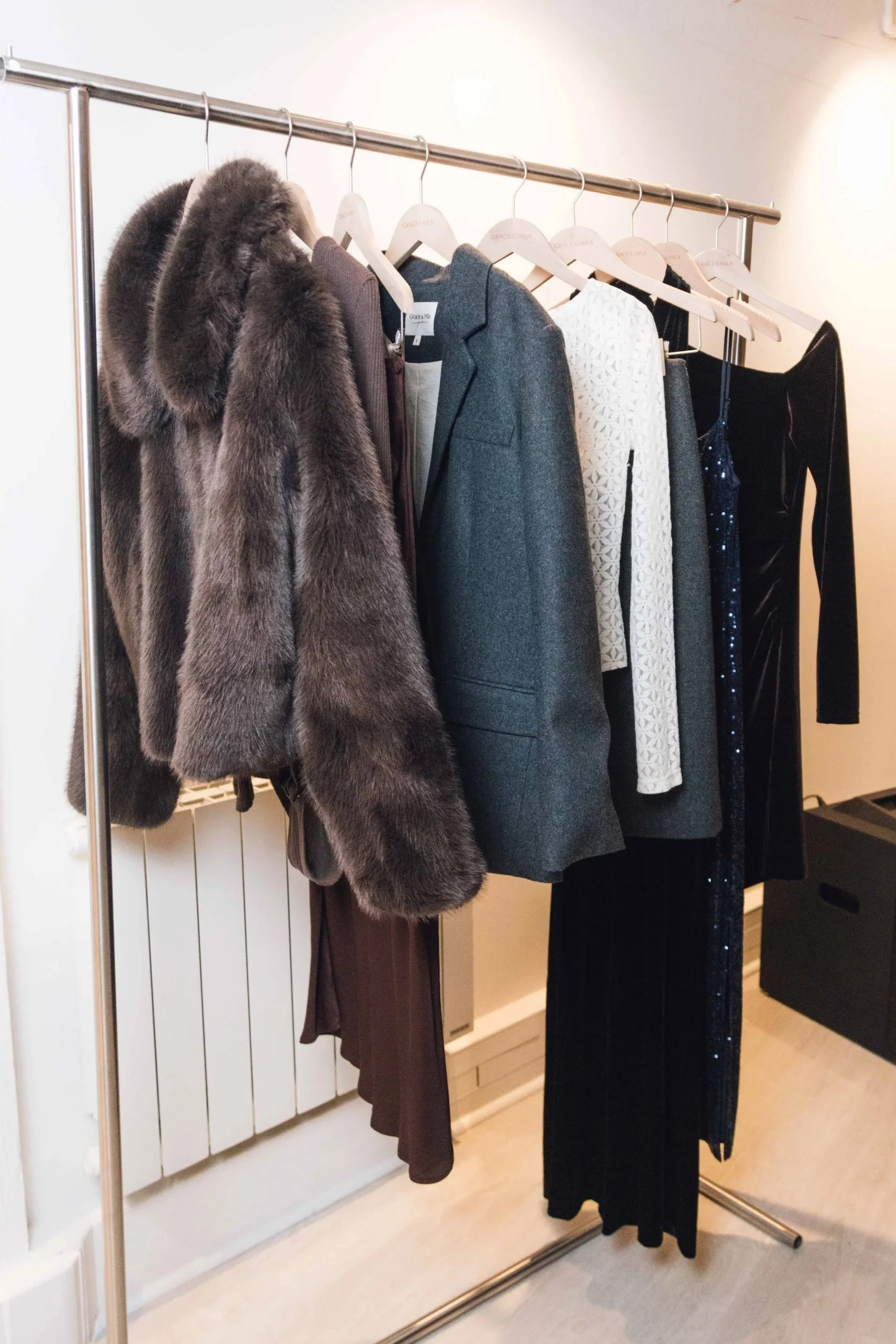 A clothing rack with luxury women's clothing, including a fur coat, blazers, dresses, and a velvet jumpsuit.